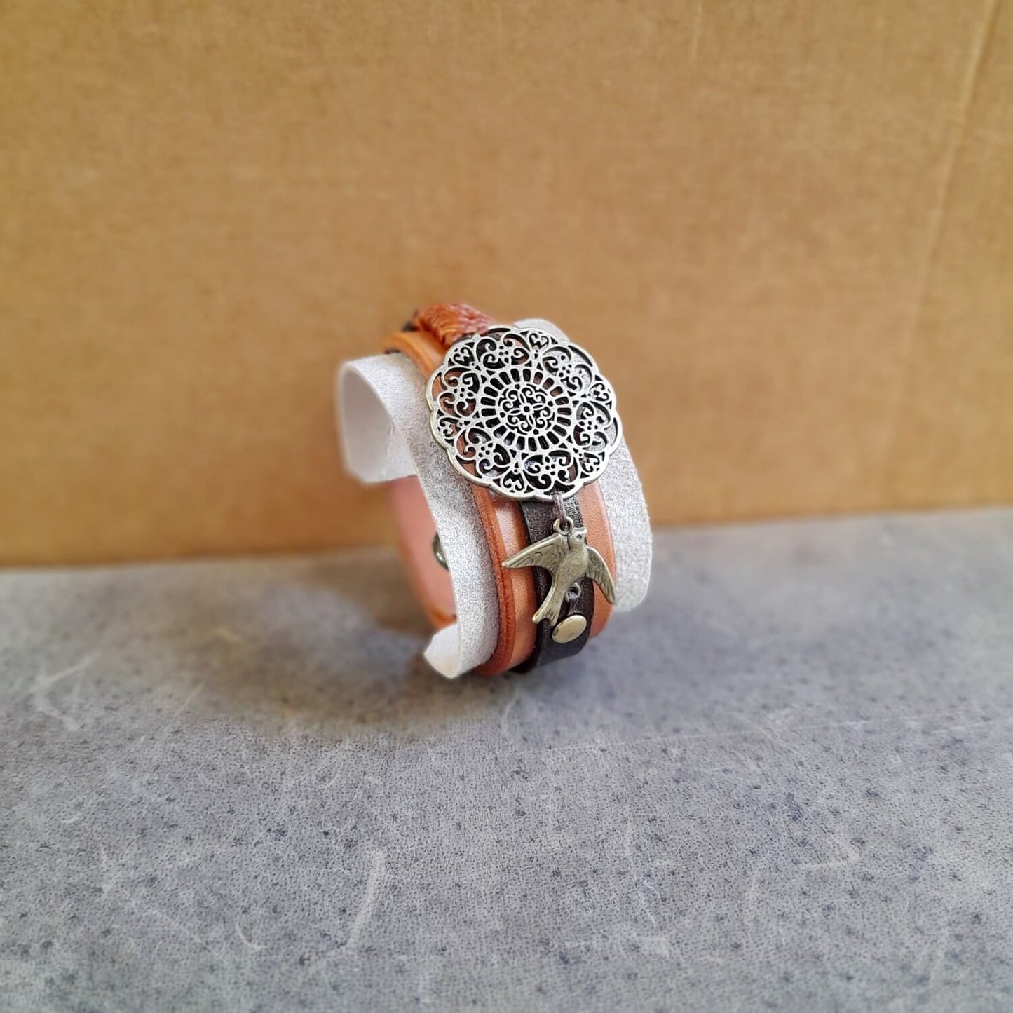 The OOAK "Happy Beige" Mandala Cuff: a wide leather and suede bracelet in neutral, earthy tones, featuring a large antique bronze mandala flower motif and a small bird charm.