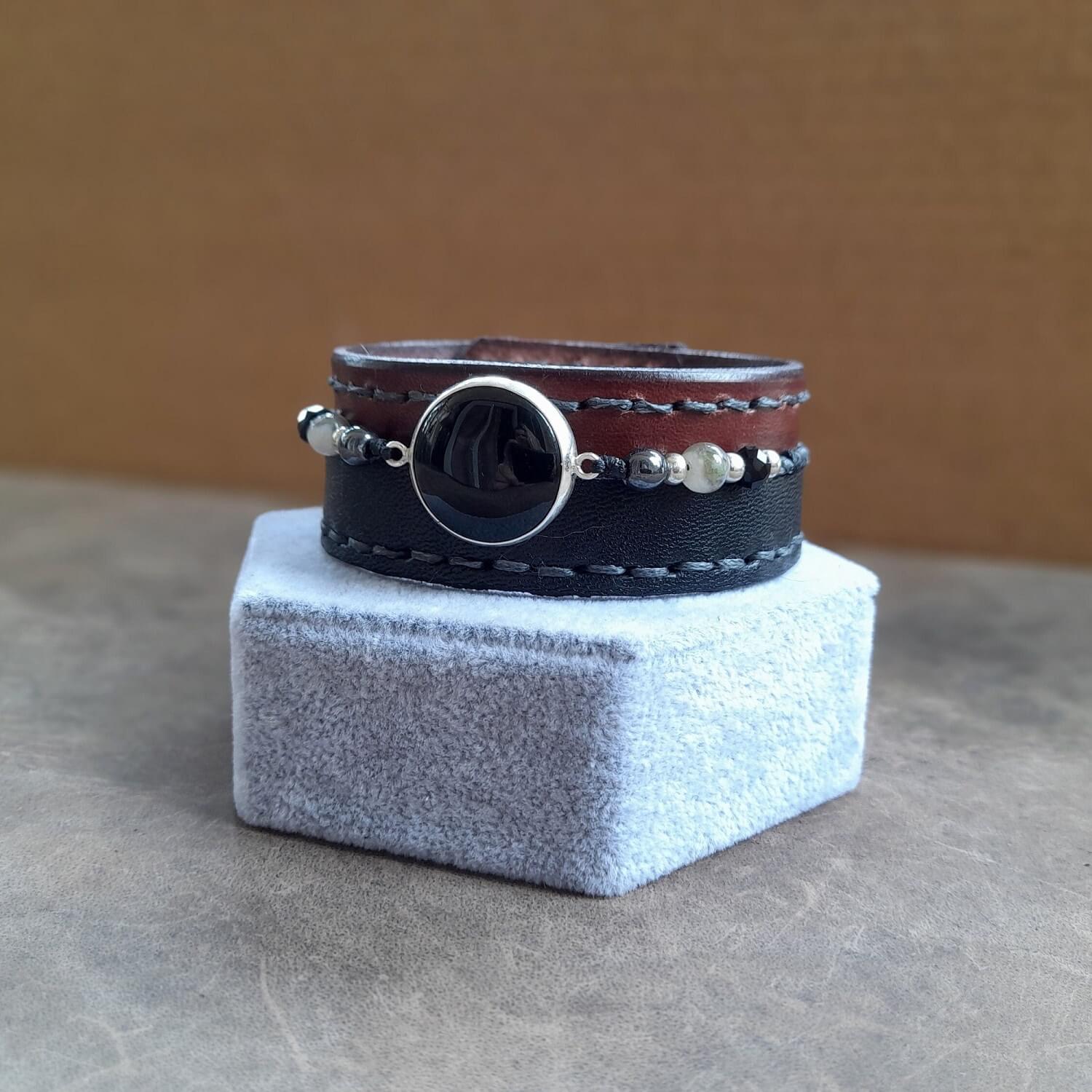 Close-up of Layered Leather & Beadwork:Close-up showing the burnished brown Vachetta leather, the black asymmetrical top leather layer, and the row of braided hematite, onyx, and smoky quartz beads on the Obsidian Power Cuff.