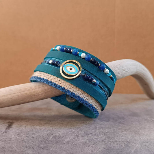 The OOAK Protector Cuff: An extra-wide petrol blue Crazy Horse leather cuff designed as a multistrand bracelet stack. Features jute, leather, and macramé strands with sodalite, lapis lazuli, turquoise, and white howlite beads, centered with a gold Evil Eye pendant.
