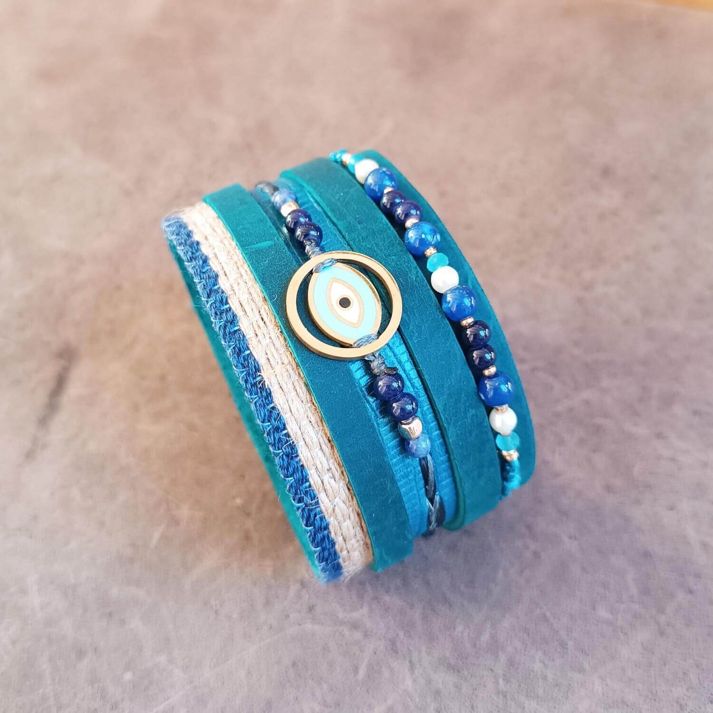 The OOAK Protector Cuff angle view: An extra-wide petrol blue Crazy Horse leather cuff designed as a multistrand bracelet stack. Features jute, leather, and macramé strands with sodalite, lapis lazuli, turquoise, and white howlite beads, centered with a gold Evil Eye pendant.