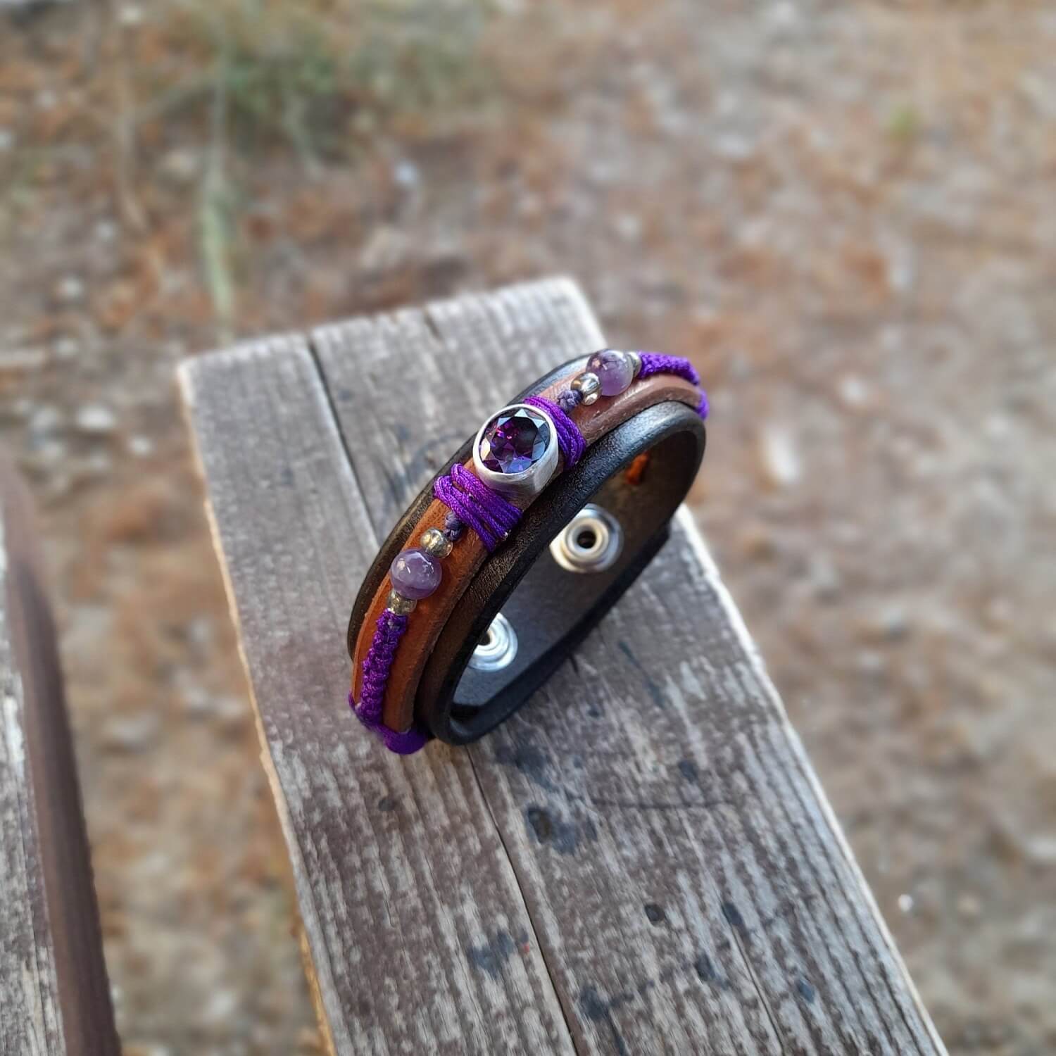The OOAK Purple Zirconia Bracelet outdoors shot: A layered dark brown and brown leather bracelet featuring a sparkling purple cubic zirconia on a sterling silver pendant, with deep purple macramé and natural amethyst beads.