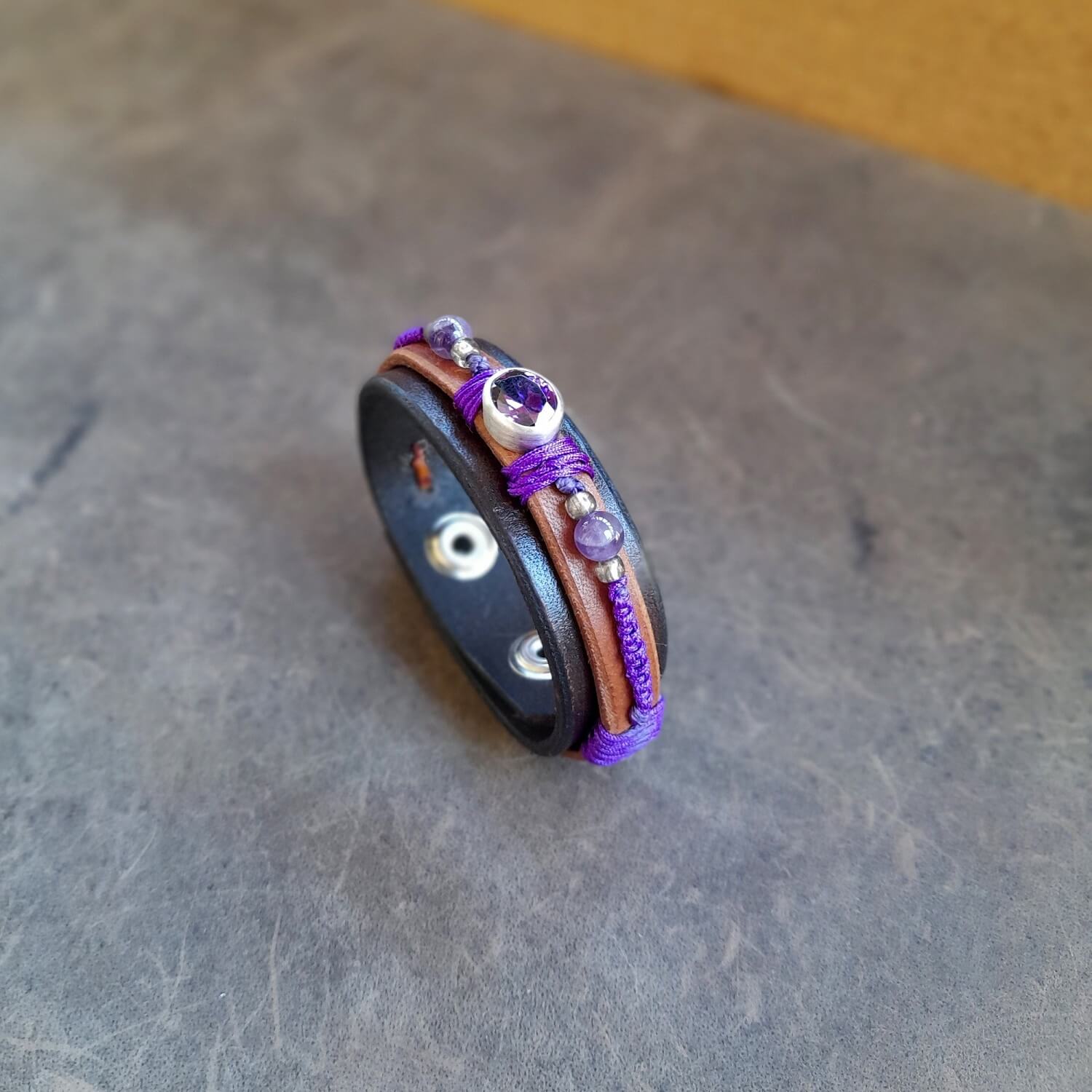 Close-up showing the two layers of dark brown and brown leather, the braided deep purple macramé cord, and the natural amethyst and silver beads on the Purple Zirconia Bracelet.