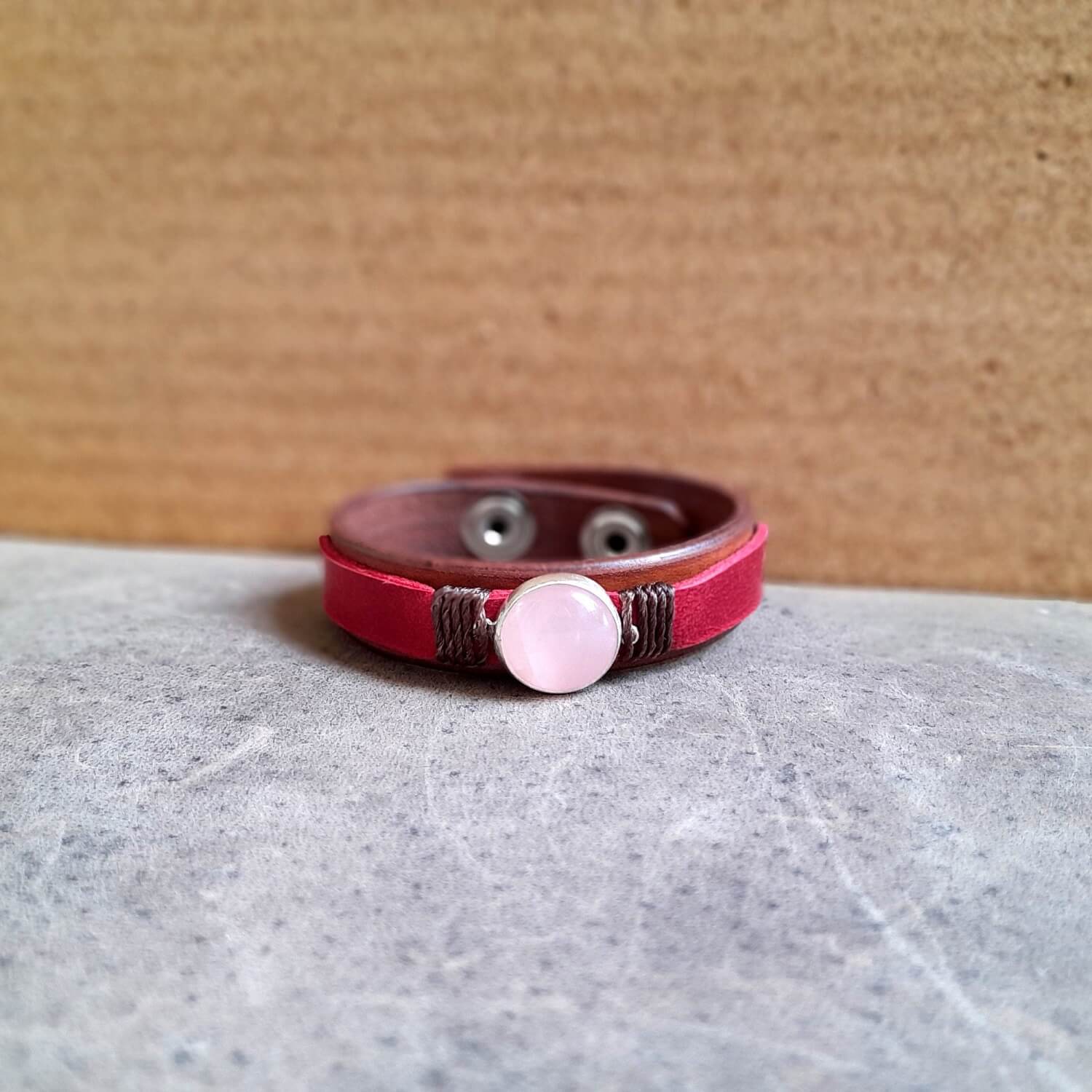 close up front view of The OOAK Red Leather Bracelet with Natural Rose Quartz: A layered brown and raspberry red full-grain leather bracelet featuring a natural rose quartz stone on a sterling silver pendant.