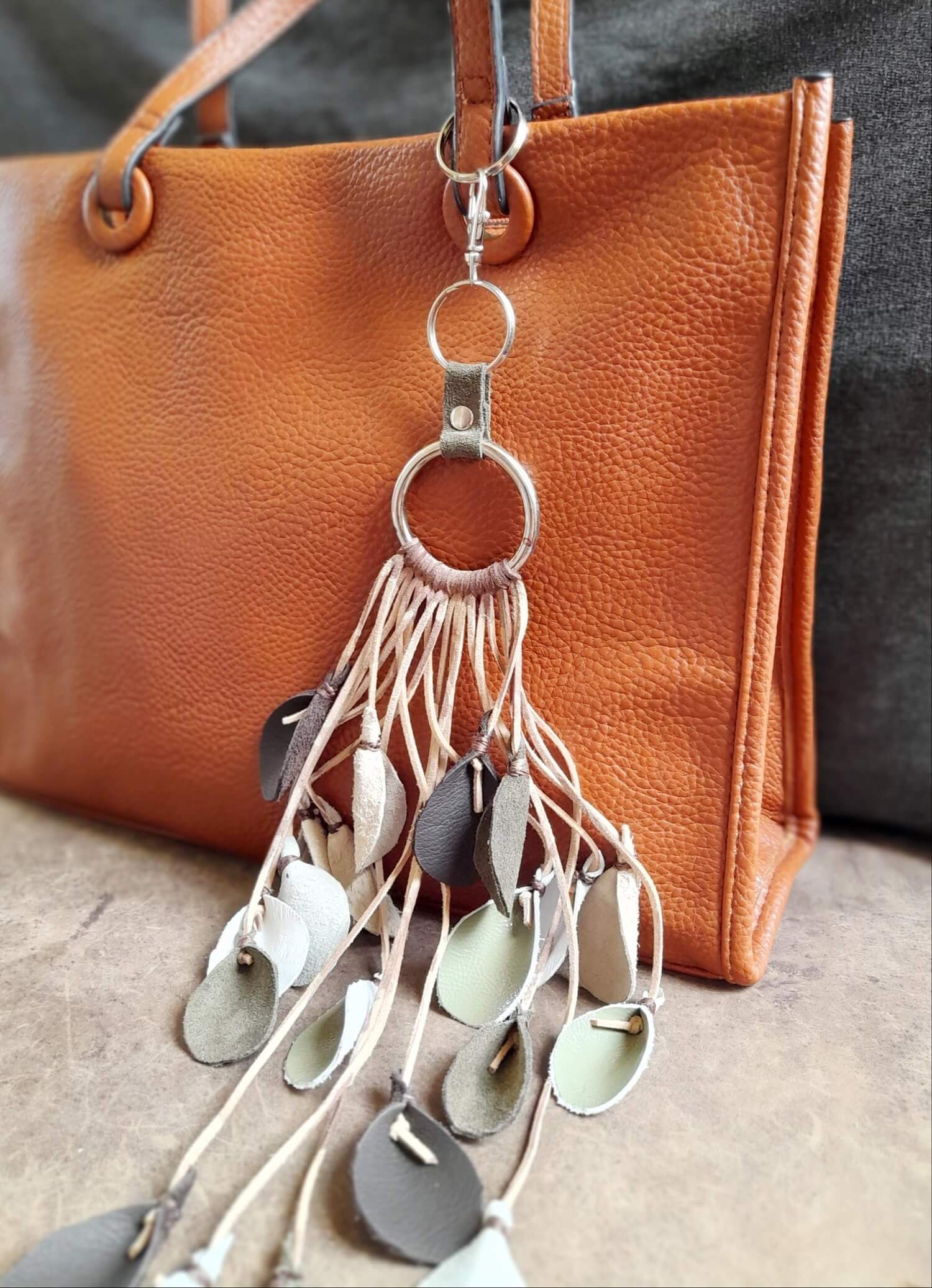 The extra-long Winter Whispers Charm clipped onto a handbag, demonstrating its fluid drape, dramatic length, and how the leather leaves hang and move.