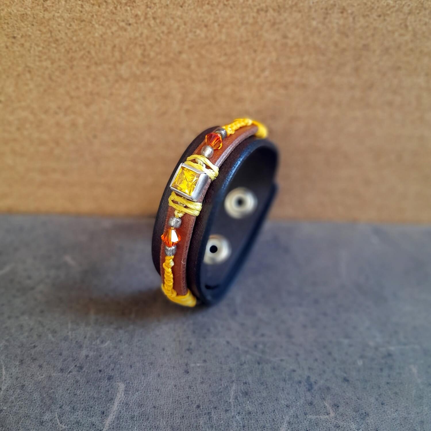 The OOAK Yellow Zirconia Bracelet: A layered dark brown and brown leather bracelet featuring a sparkling yellow cubic zirconia on a sterling silver pendant, with yolk yellow macramé and orange crystal beads.