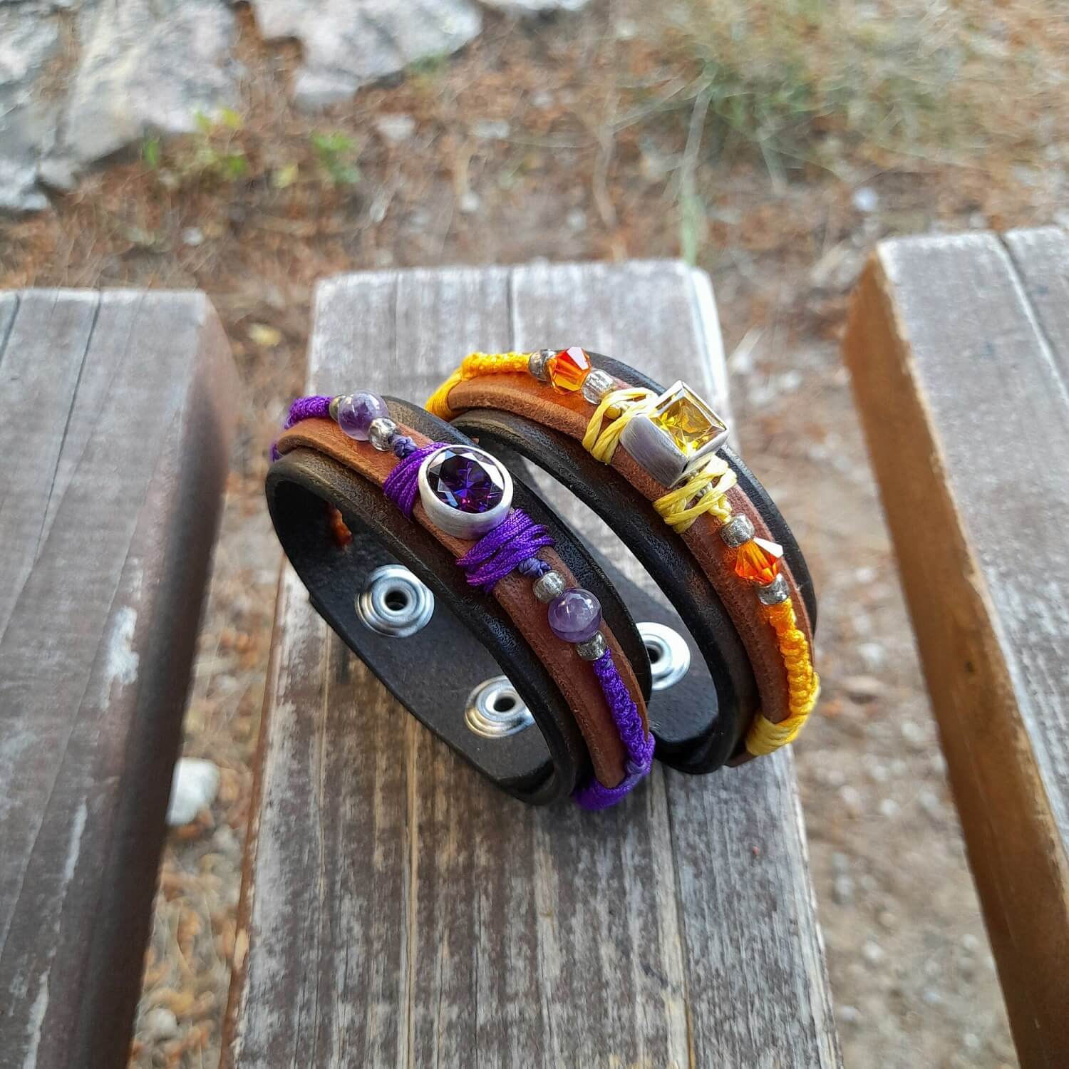 The OOAK Yellow Zirconia Bracelet next to its purple sibling: A layered dark brown and brown leather bracelet featuring a sparkling yellow cubic zirconia on a sterling silver pendant, with yolk yellow macramé and orange crystal beads.