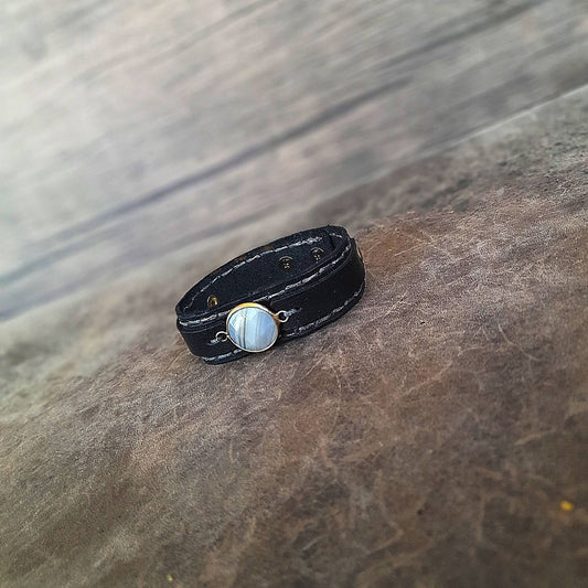 The Obsidian Cuff: An OOAK men's black leather bracelet featuring a gold-plated agate cabochon with light and dark gray veins, and deep gray hand-stitched details.