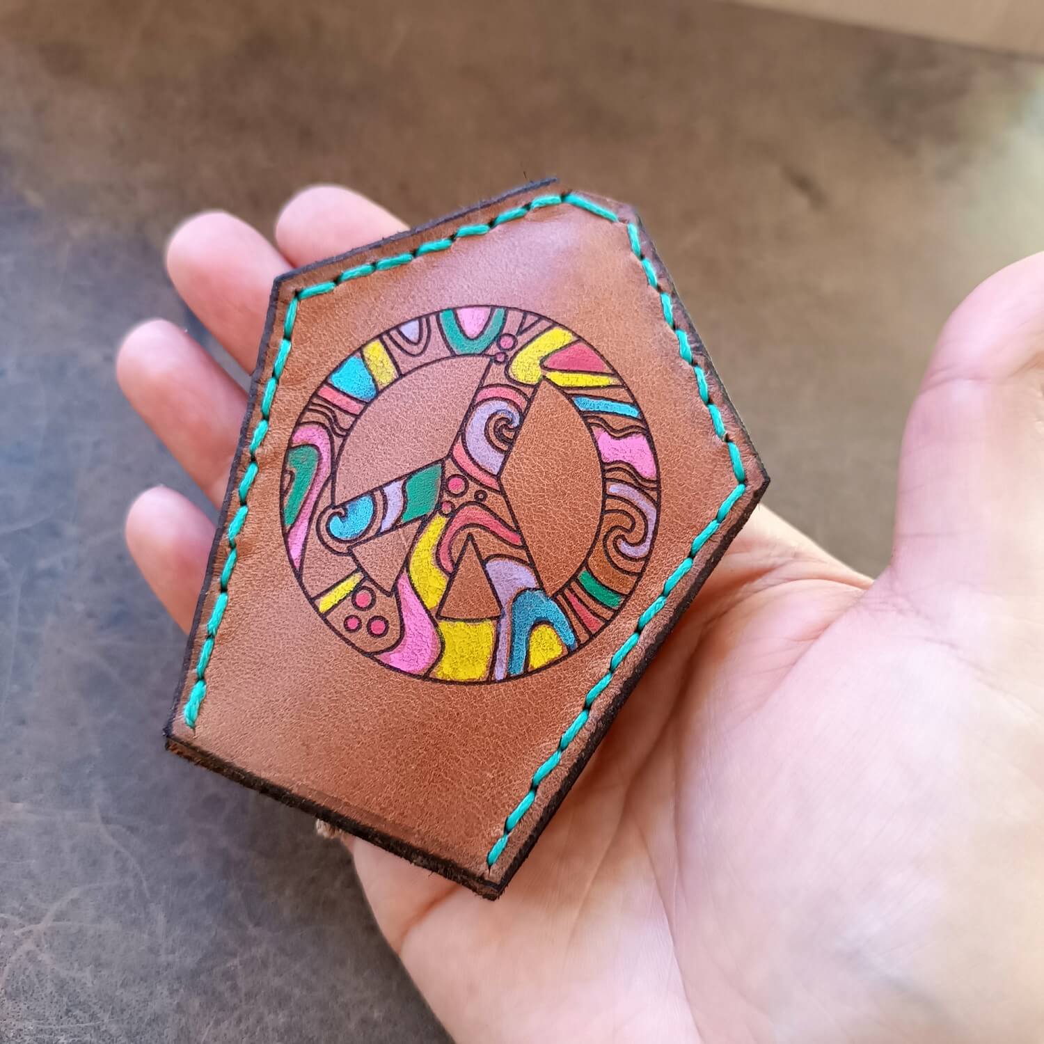 Detailed close-up of the large peace symbol on The Peace Weaver Key Holder held on hand, highlighting the vibrant hand-painted abstract patterns and the texture of the Vachetta leather.