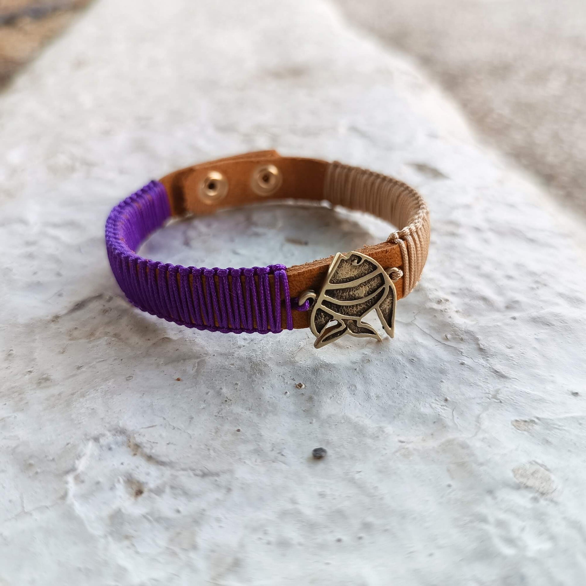 Bracelet with purple cord and brown leather strap on a textured surface