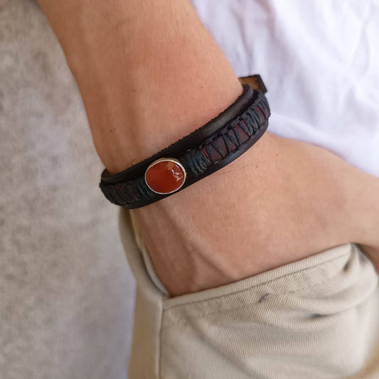 The Roamer Leather Bracelet worn on a man's wrist, showcasing its layered design, dark leather tones, and the subtle pop of the red Carnelian gemstone, fitting comfortably.