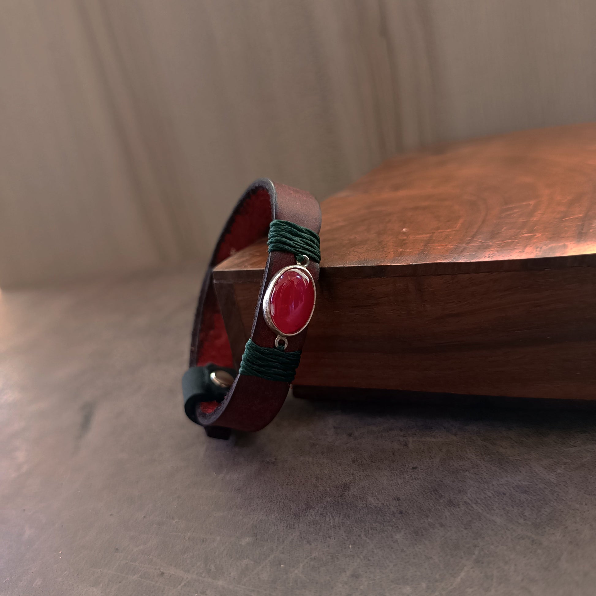 Close up Side view of the dark red Crazy Horse leather texture and the deep forest green waxed cord wrap on The Rooted Glow Bracelet, showing the quality and contrast of materials.