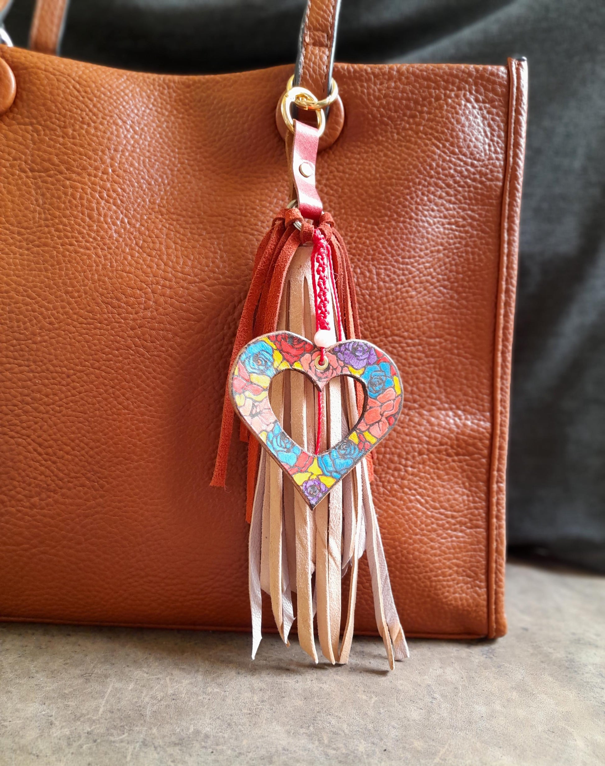 The Stained Glass Heart Charm clipped onto a bag, demonstrating its size, vibrant colors, artistic detail, and how it drapes elegantly.