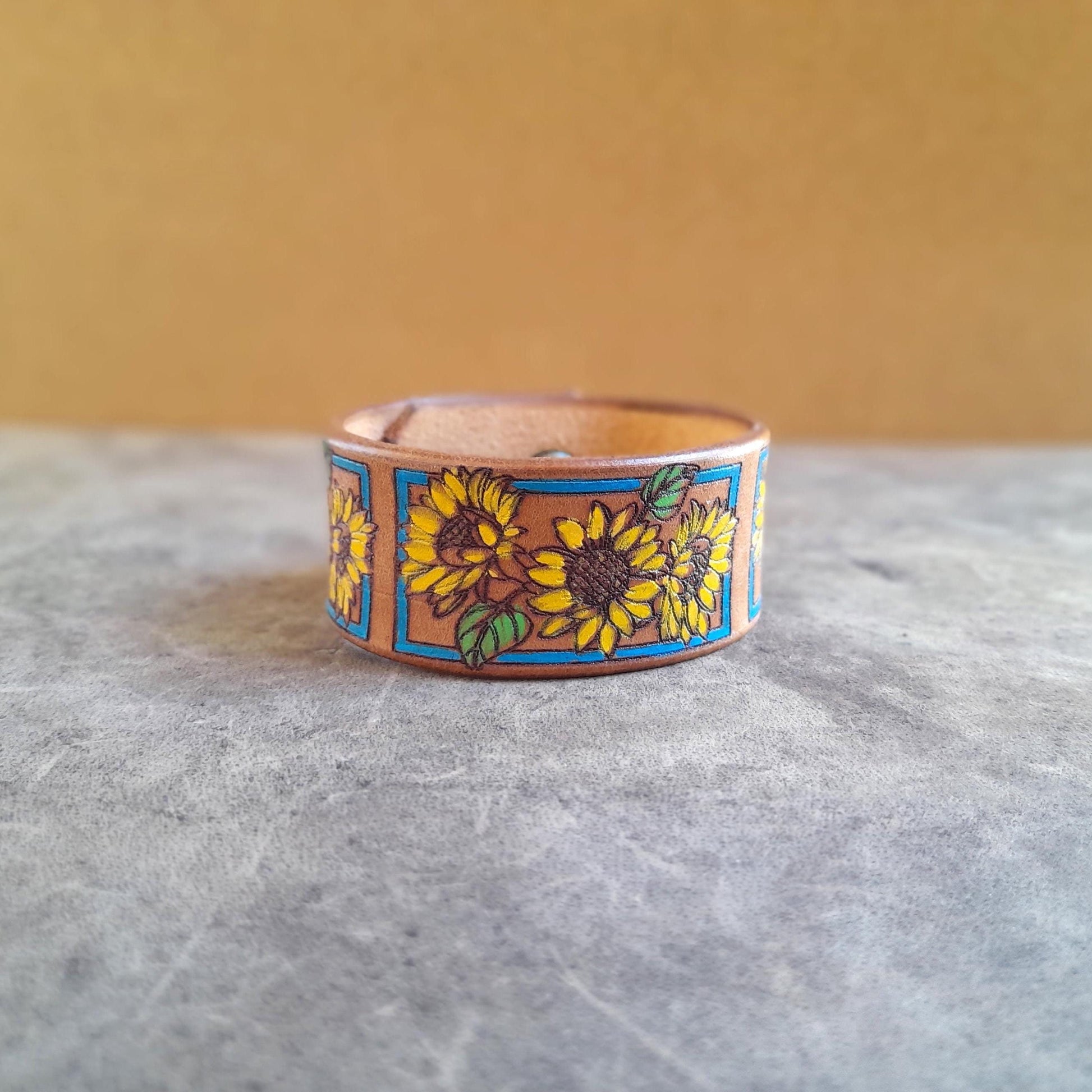 The Sunshine Bloom Leather Cuff Bracelet from Lucky Seven Leather. Features a hand-painted vintage sunflower pattern in yellow, orange, and turquoise on a mustard brown Crazy Horse leather cuff.