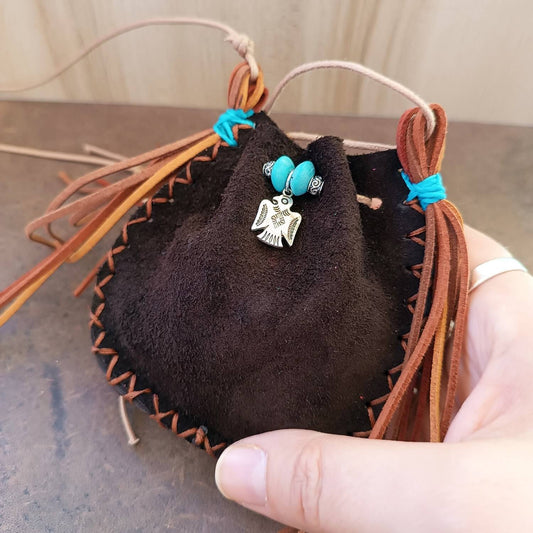 The Thunderbird Keeper Neck Pouch held on hand, showcasing its size, featuring the silver Thunderbird and suede tassels.