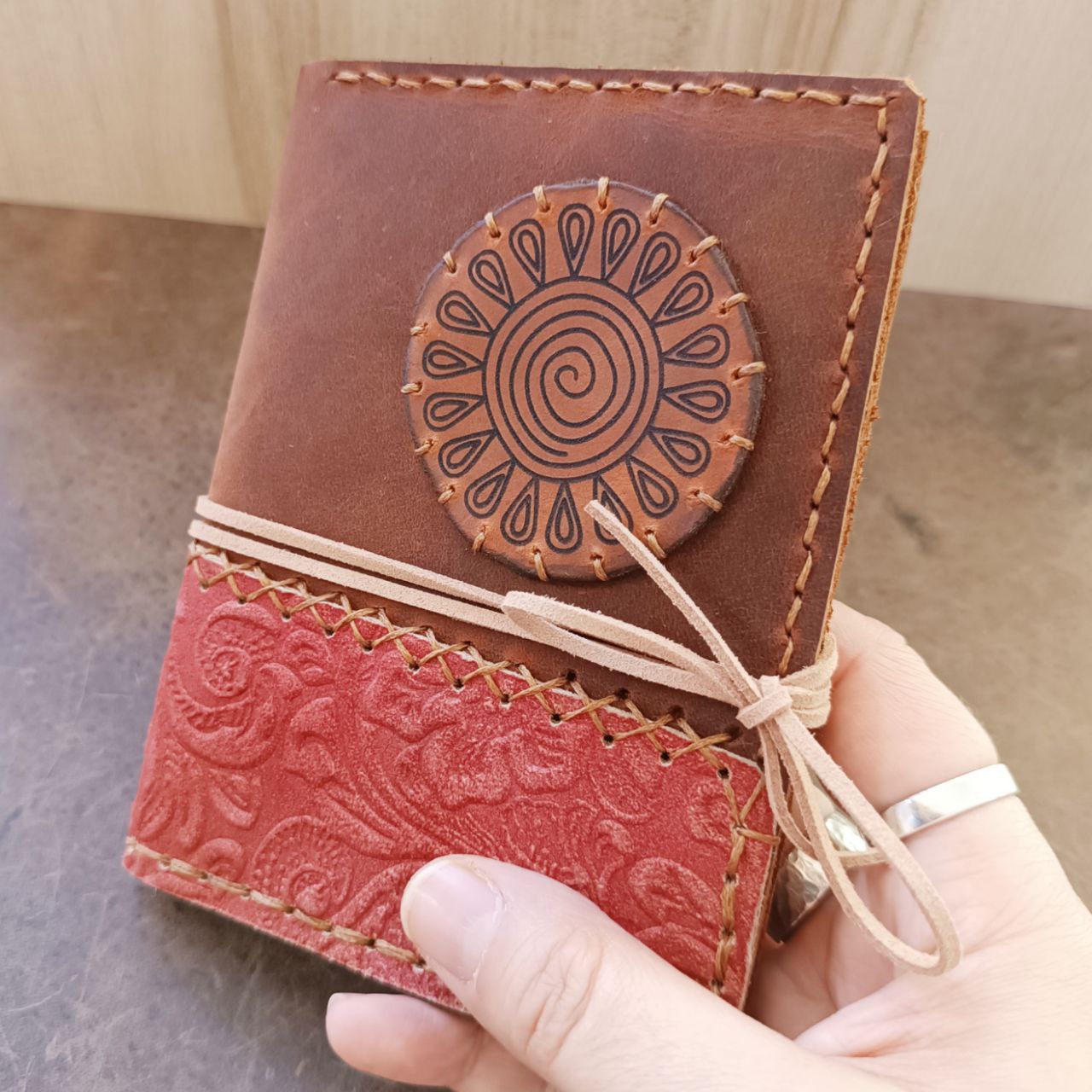 Detailed close-up of the hand-stitched spiral sun and embossed brick-red floral leather on The Wanderer's Journal passport case, highlighting the unique texture and craftsmanship.