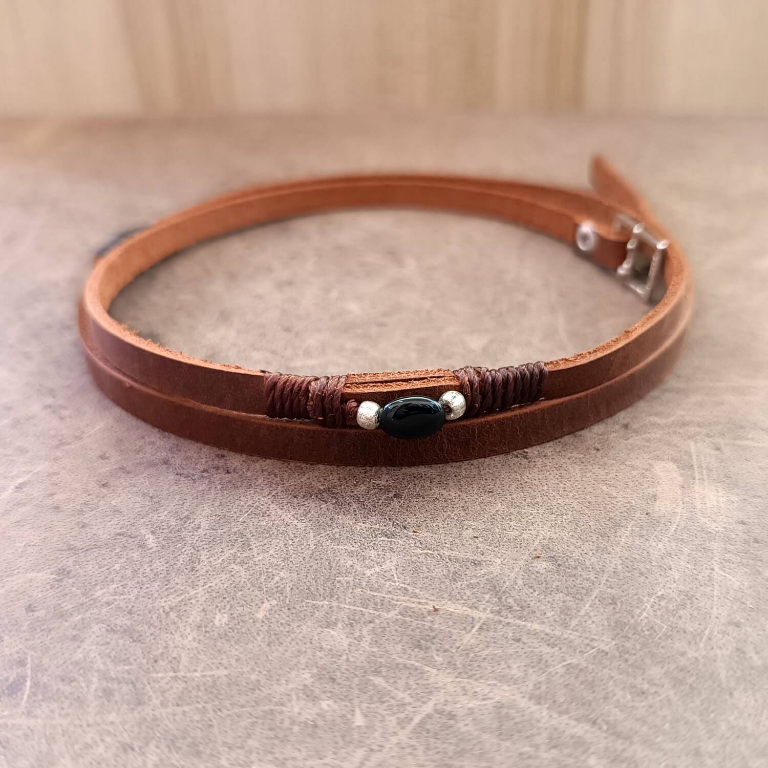 The Wanderer's Wrap shown as a double-wrap choker necklace, showing the dark brown Crazy Horse leather and the Black Tourmaline stone.