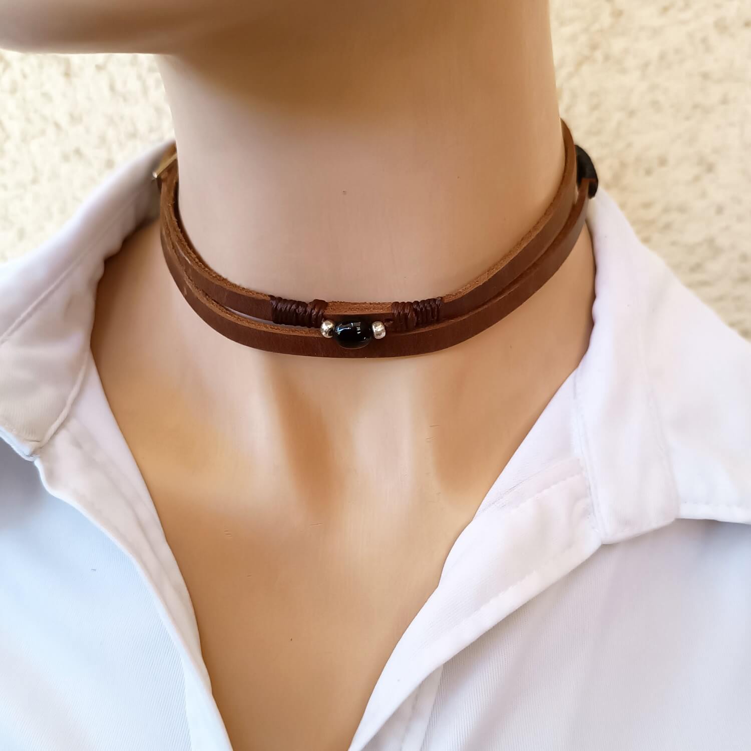 The Wanderer's Wrap worn as a double-wrap choker necklace, showing the dark brown Crazy Horse leather and the Black Tourmaline stone resting on the neck.