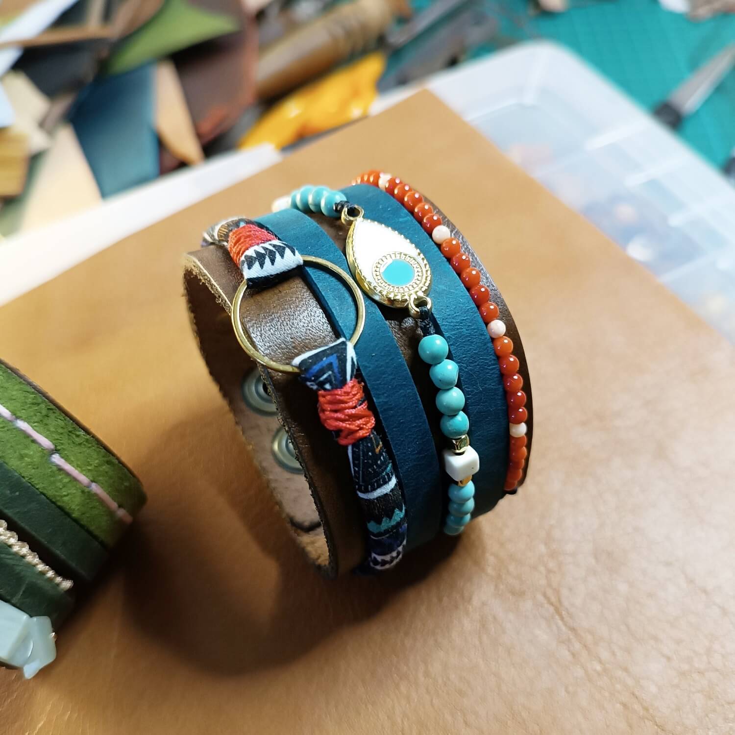 close-up after making: the red crystal, white howlite, and natural turquoise beads, and the brass enamel evil eye charm on The Warrior Stack leather cuff, highlighting their colors and textures.
