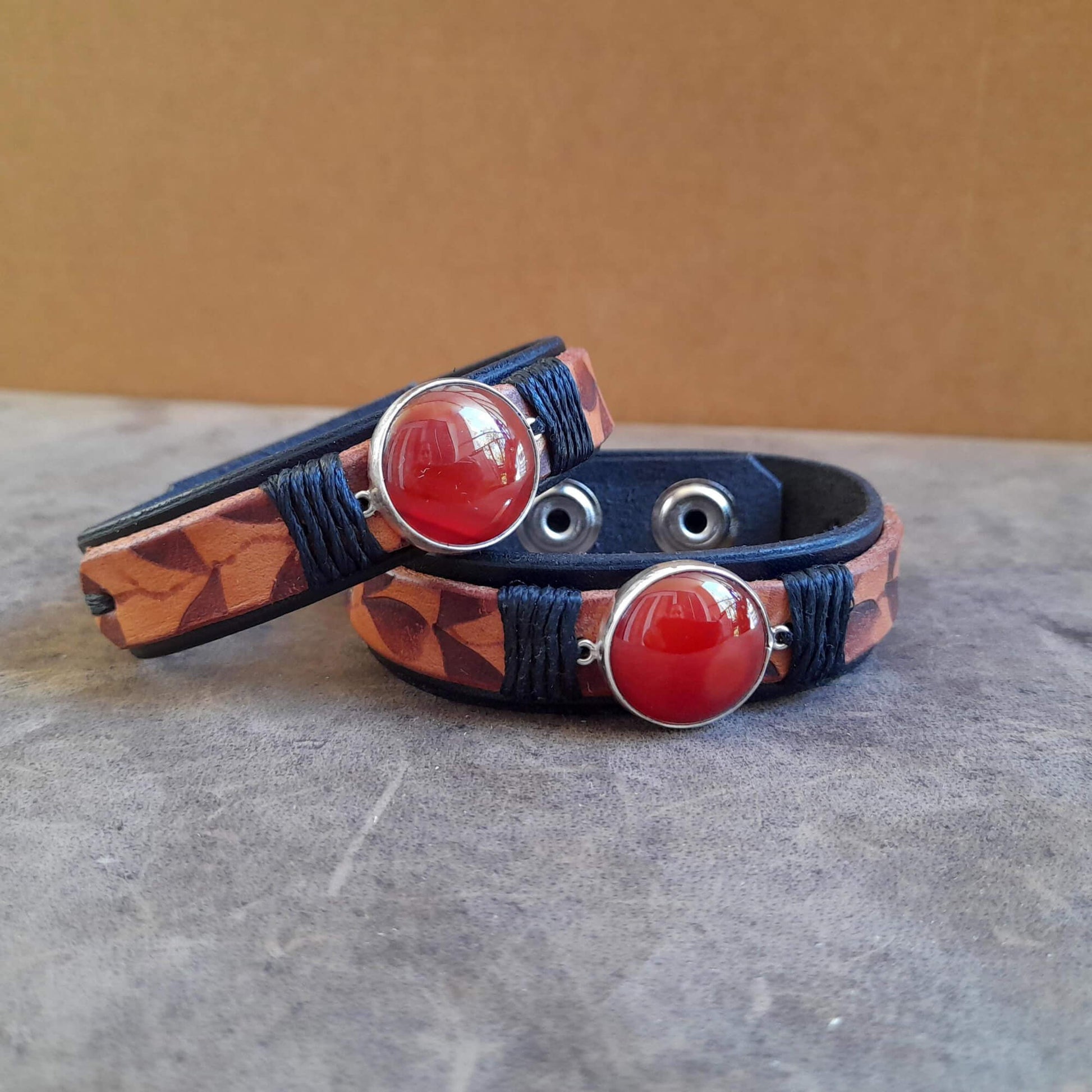 Close up of Two Ember Bloom Cuffs displayed side-by-side, showcasing them as a matching pair. Both bracelets feature hand-pyrographed leather and Red Carnelian in sterling silver pendants.