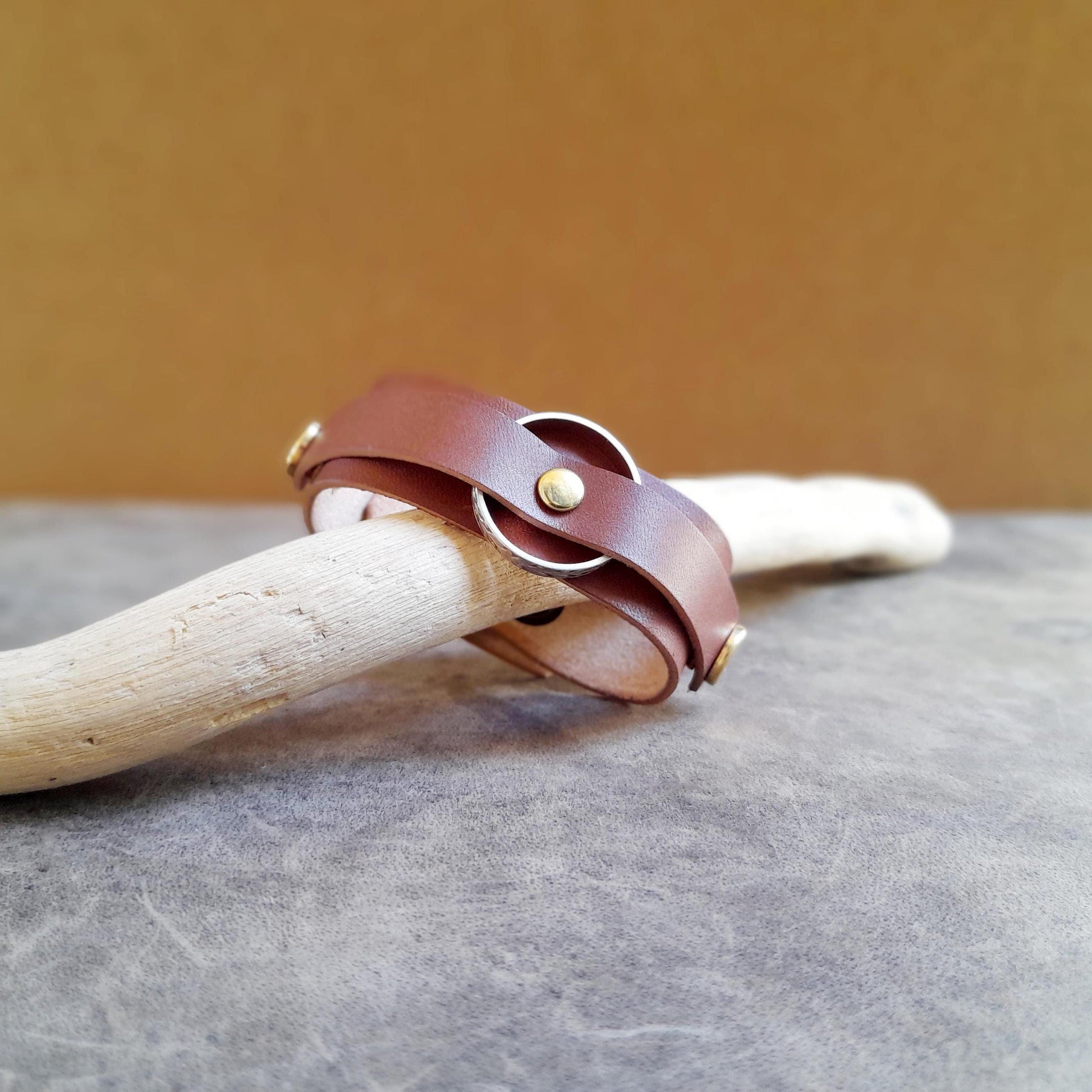 Vachetta Leather Ring Holder Bracelet in brown with gold clasps, carrying a gold ring.