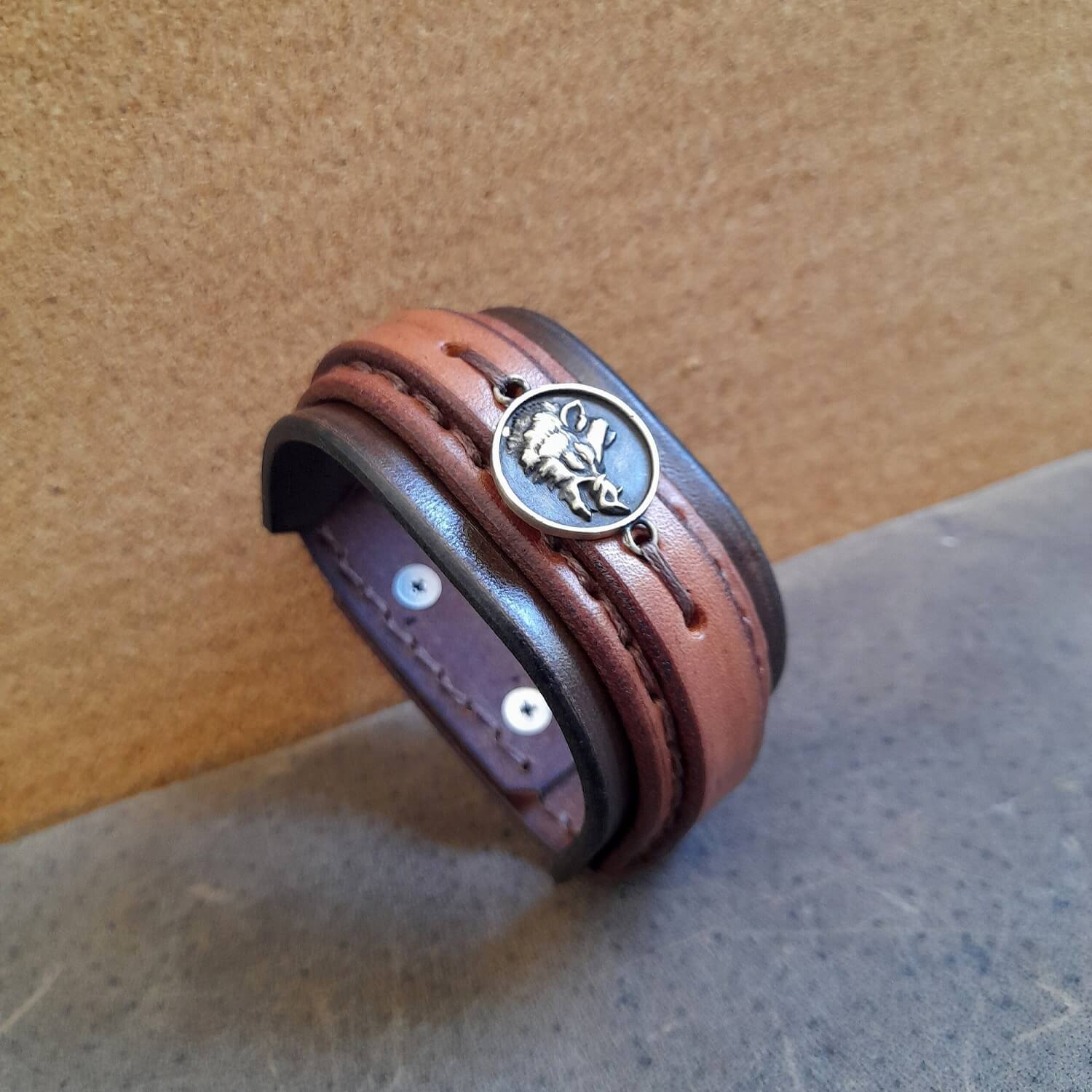 Brown leather cuff bracelet with a metal clasp on a textured surface