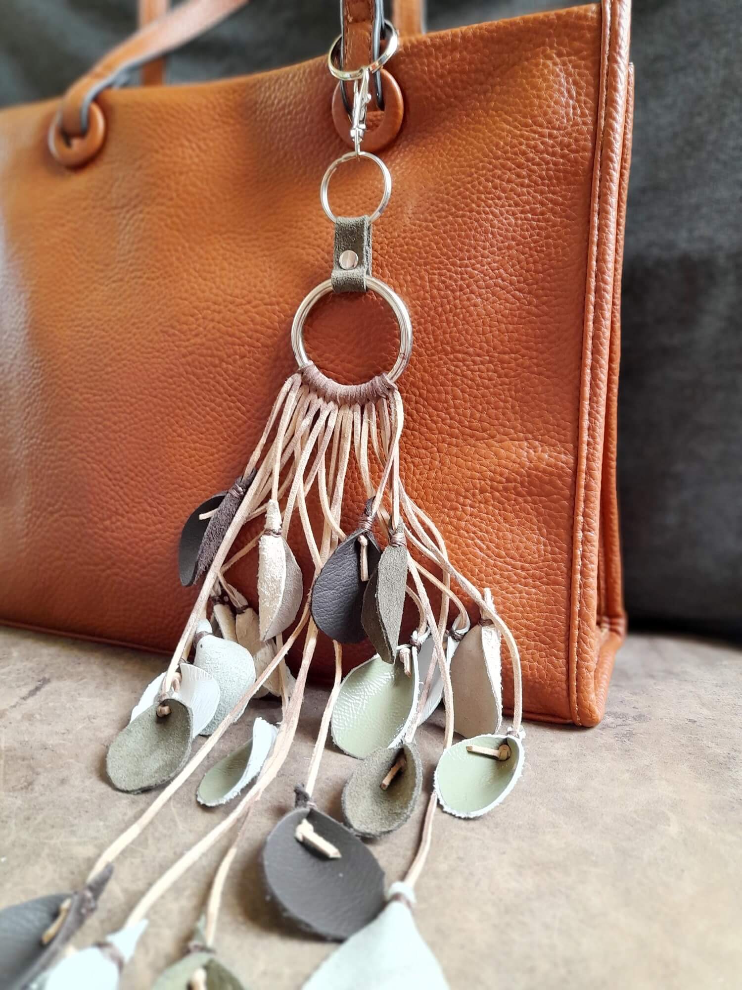 The extra-long Winter Whispers Charm clipped onto a handbag, demonstrating its fluid drape, dramatic length, and how the leather leaves hang and move.