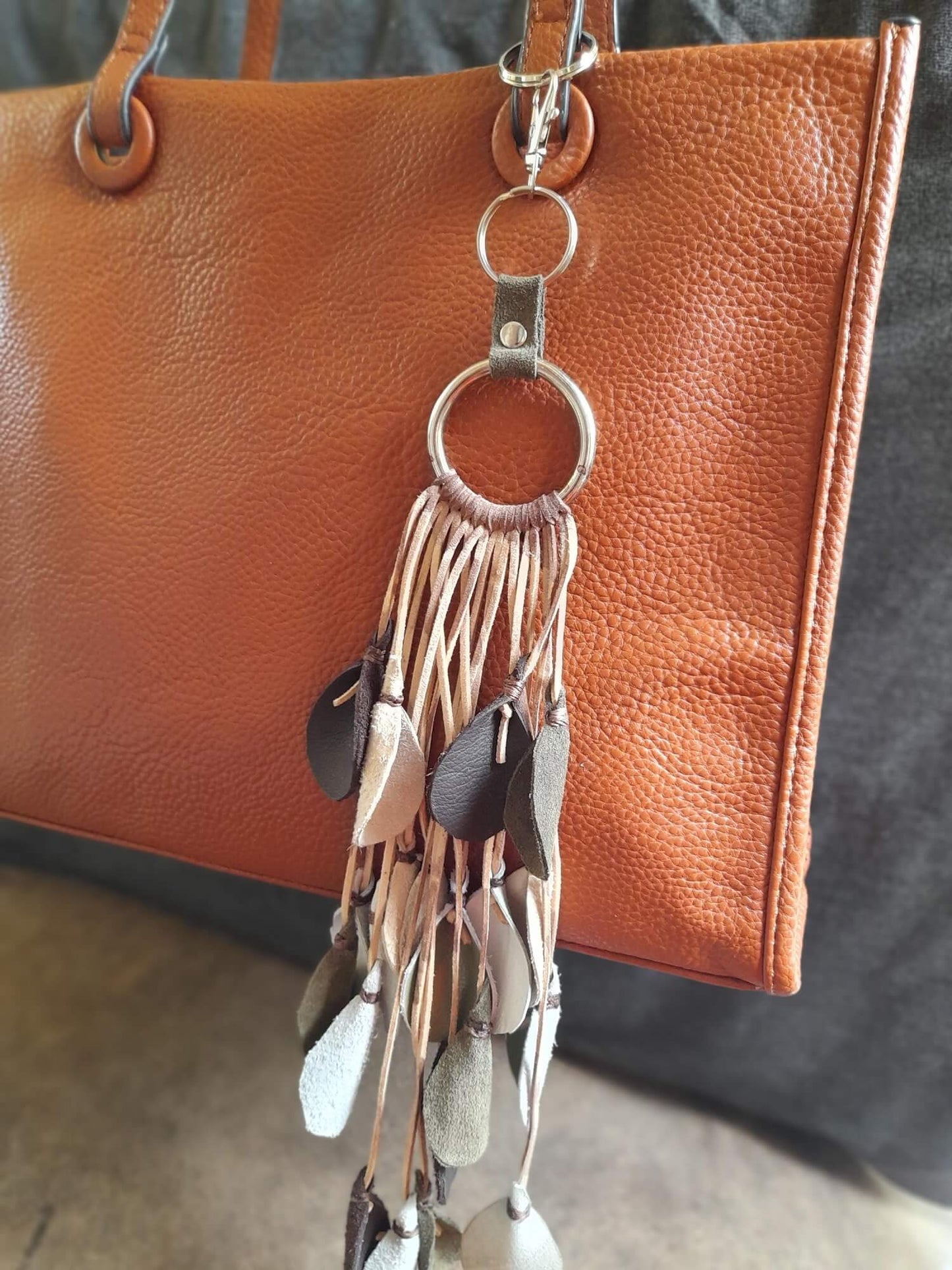 Brown leather handbag with a keychain featuring tassels and a ring.