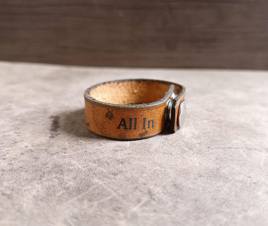 Brown leather bracelet with 'All In' engraving on a gray surface