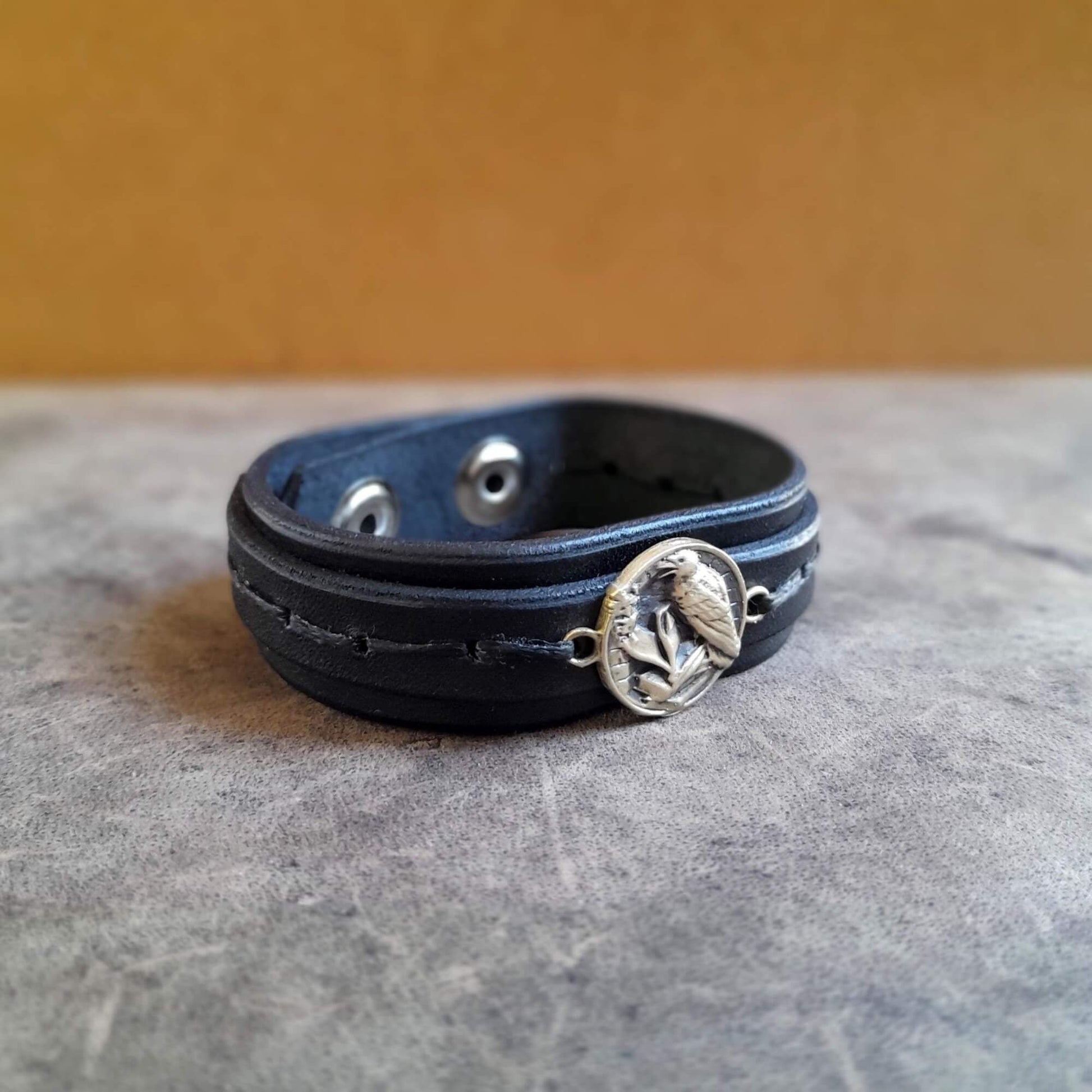 Total Black leather bracelet with a brass raven emblem on a textured surface