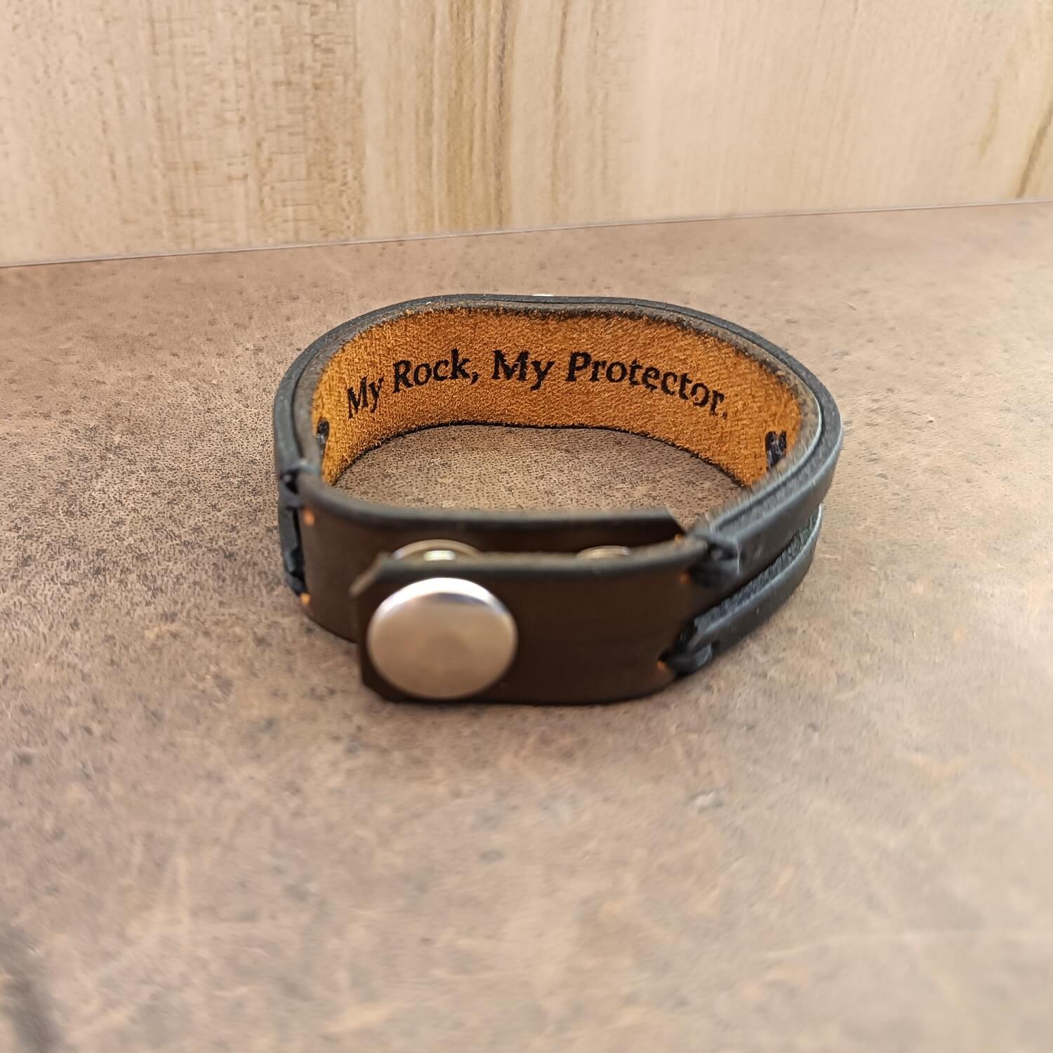 Adjustable snap button and leather detail of the Archangel bracelet closure, showing the engraved underside message