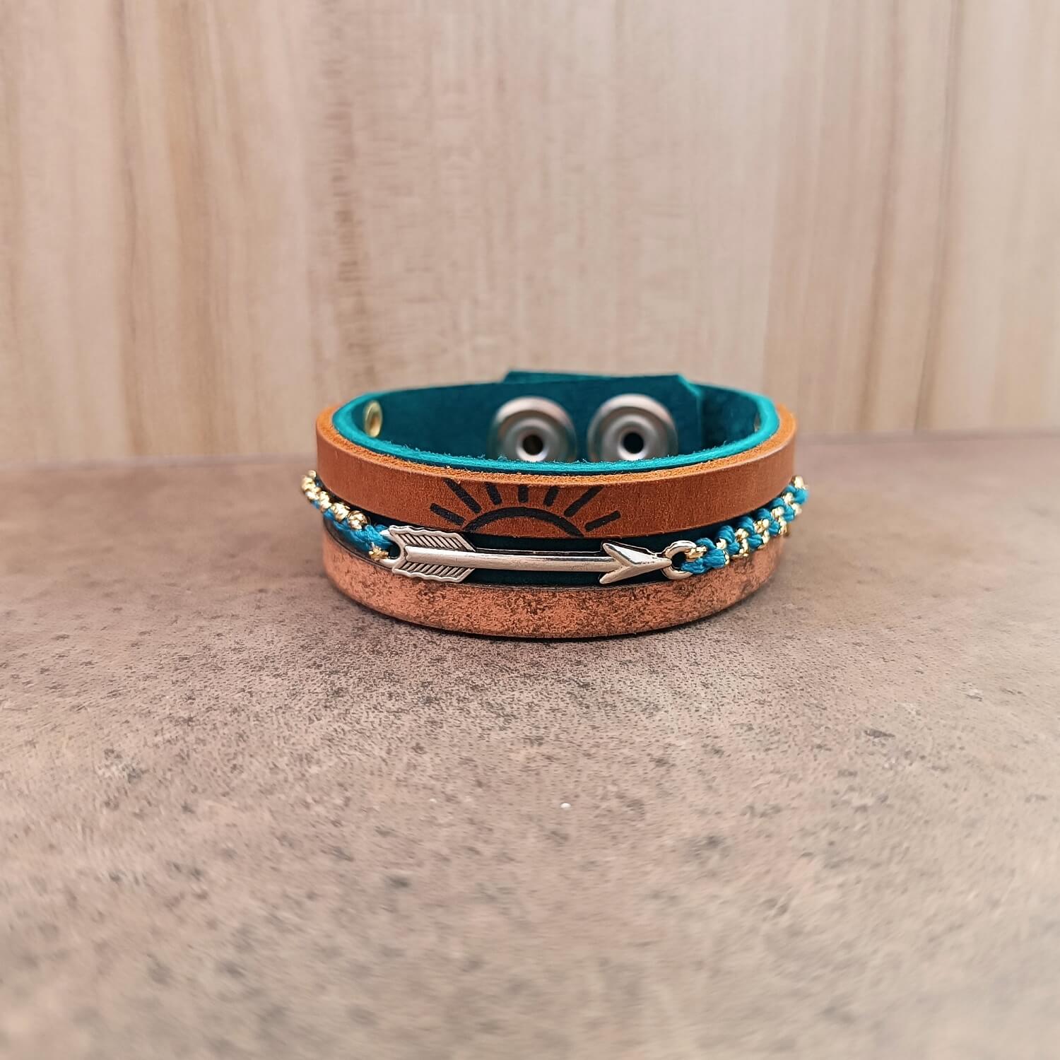 Handmade layered and multistrand leather bracelet with sun and arrow designs on a wooden surface