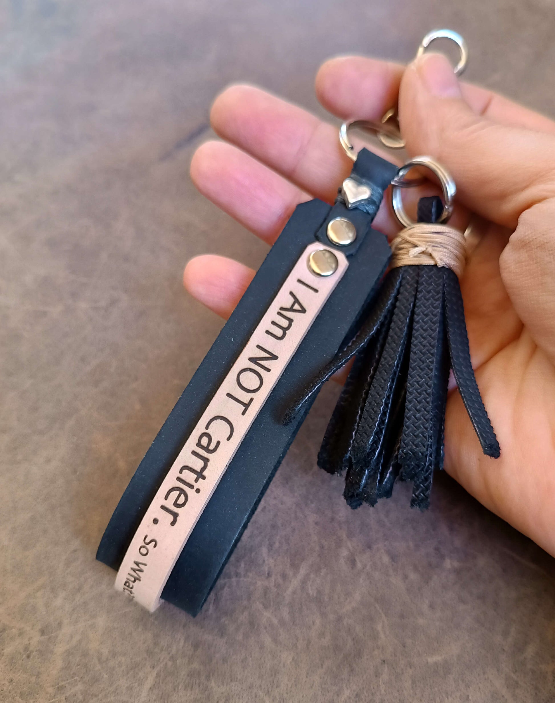 Keychain with tassel and engraved text held in a hand against a neutral background