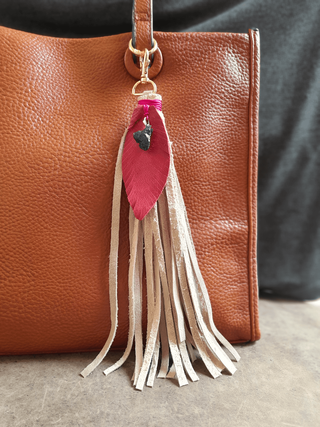 Brown leather handbag with a tassel keychain featuring a pink feather and beige fringe.