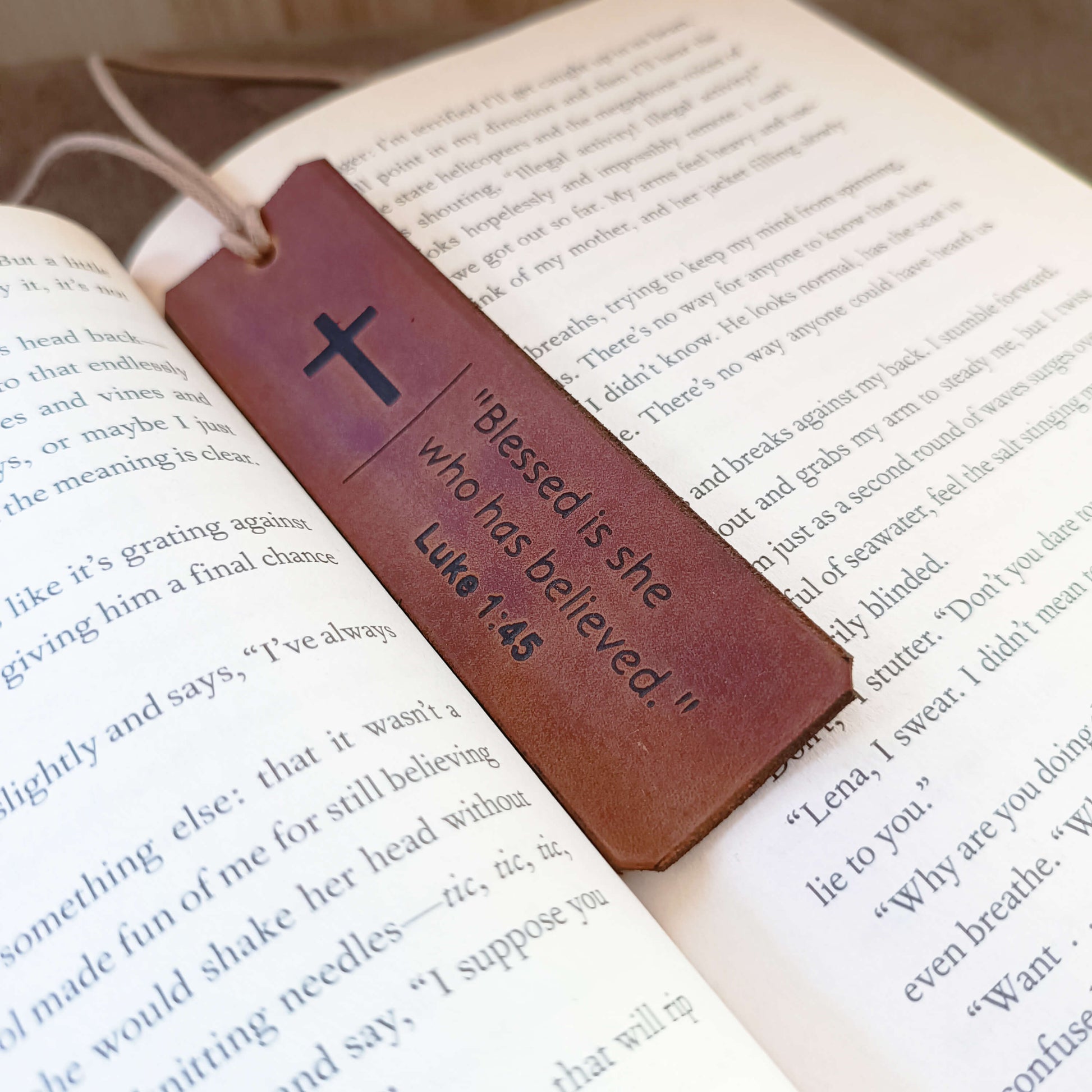 Leather bookmark with cross and Bible verse on an open book