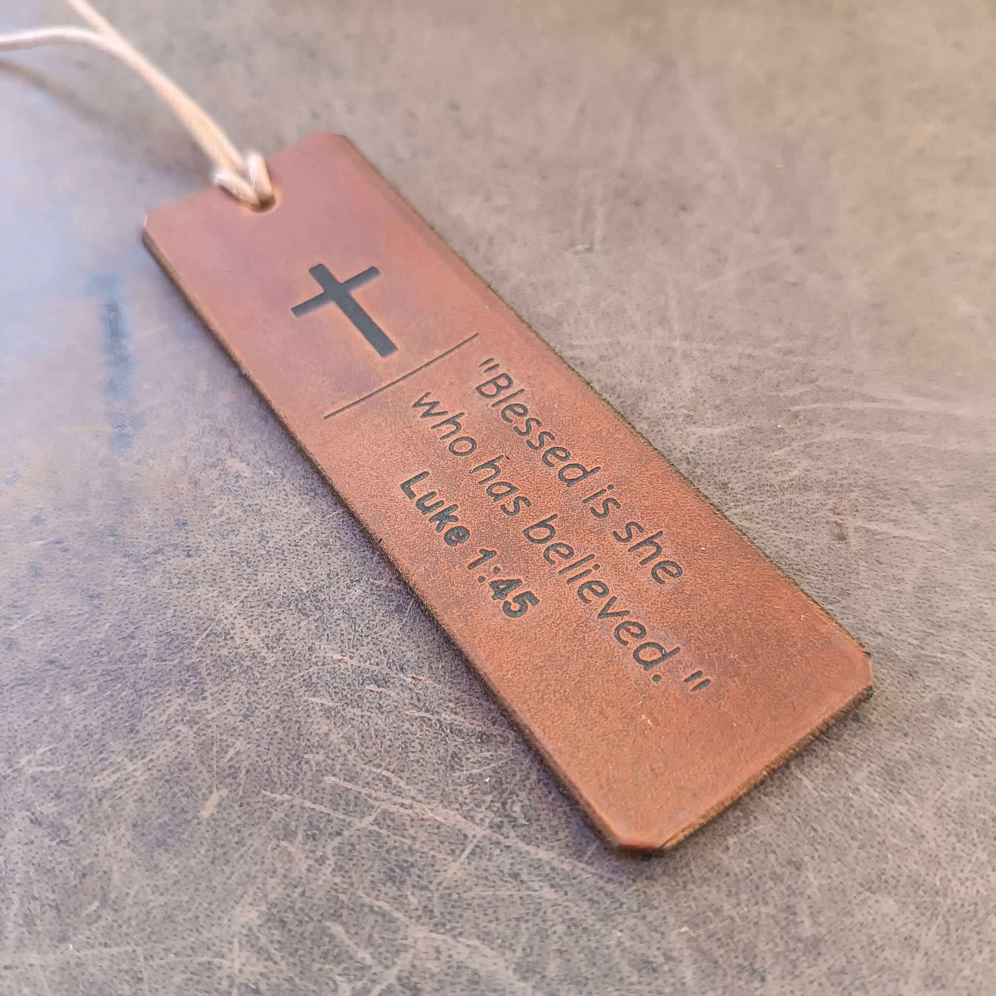 Brown leather bookmark with cross and Bible verse on a textured surface