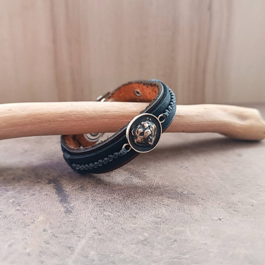 Black leather bracelet with a bear pendant on a wooden stick against a beige background