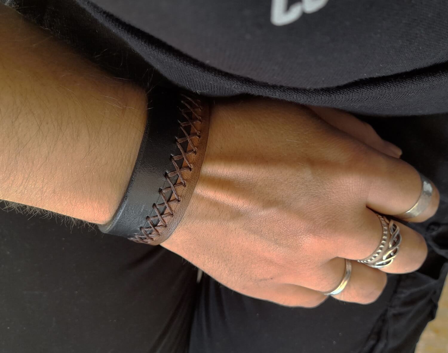 Close-up of a person's wrist wearing a black brown leather bracelet with X stitching.