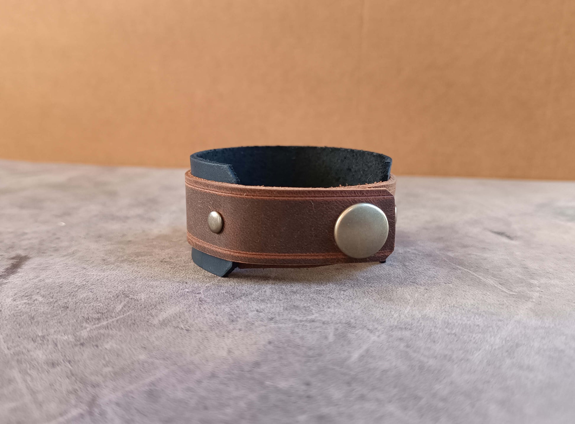 Brown leather bracelet with a silver button on a gray surface