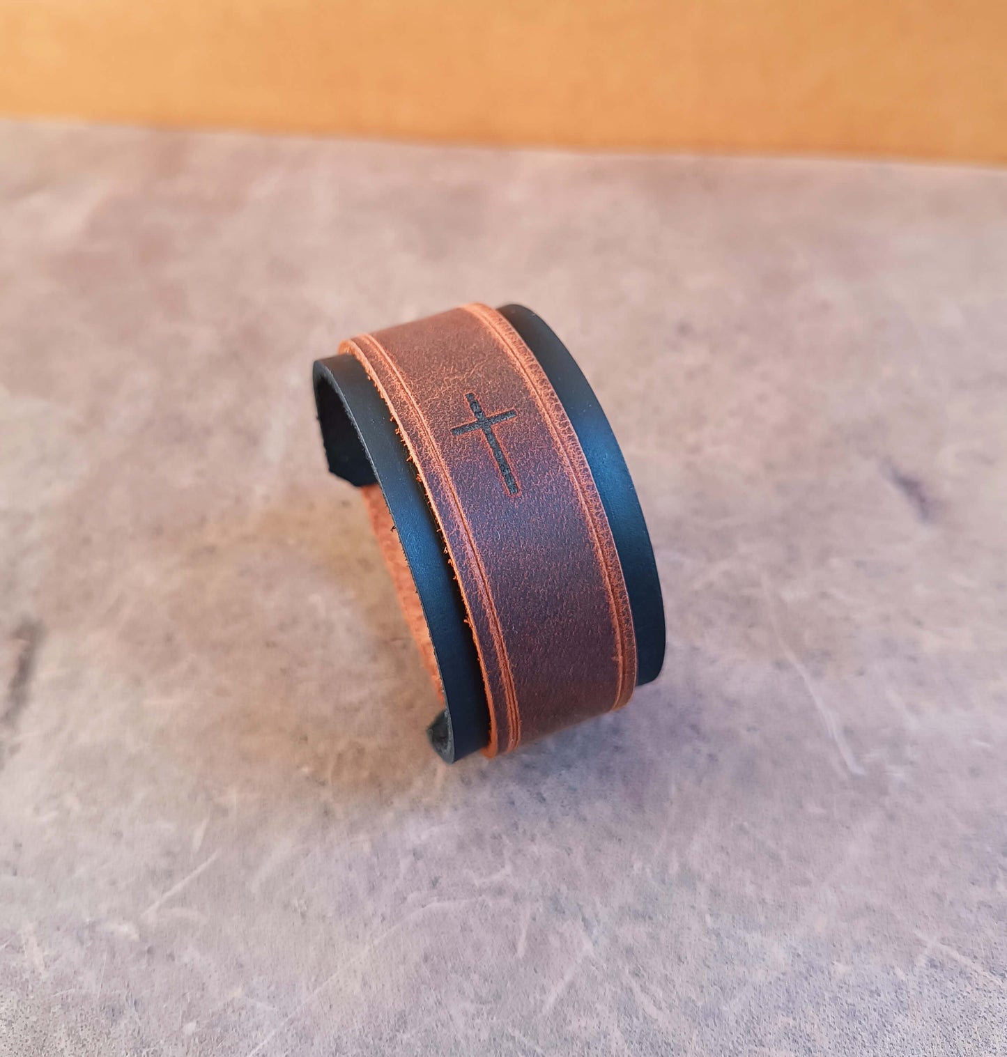Brown leather cuff with a cross design on a textured surface