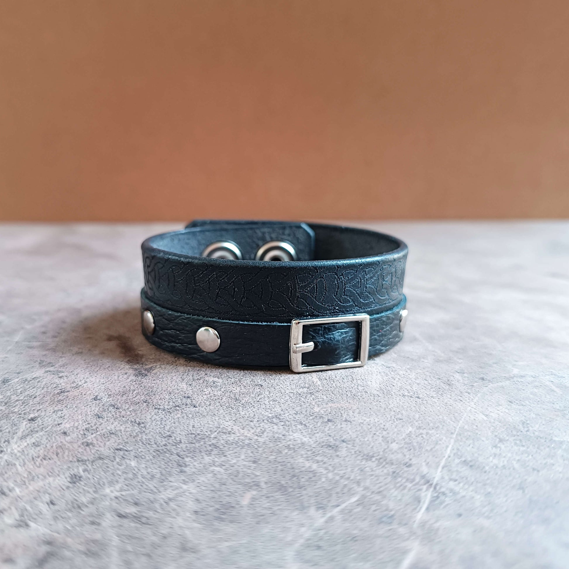 Black leather bracelet with silver buckles on a textured surface