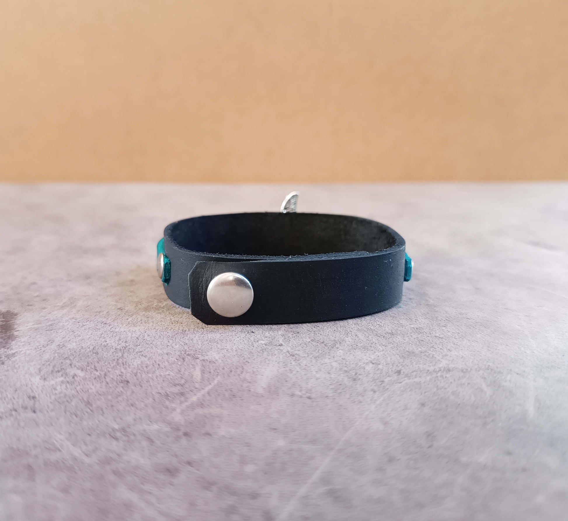 Black leather bracelet with a silver button on a textured surface