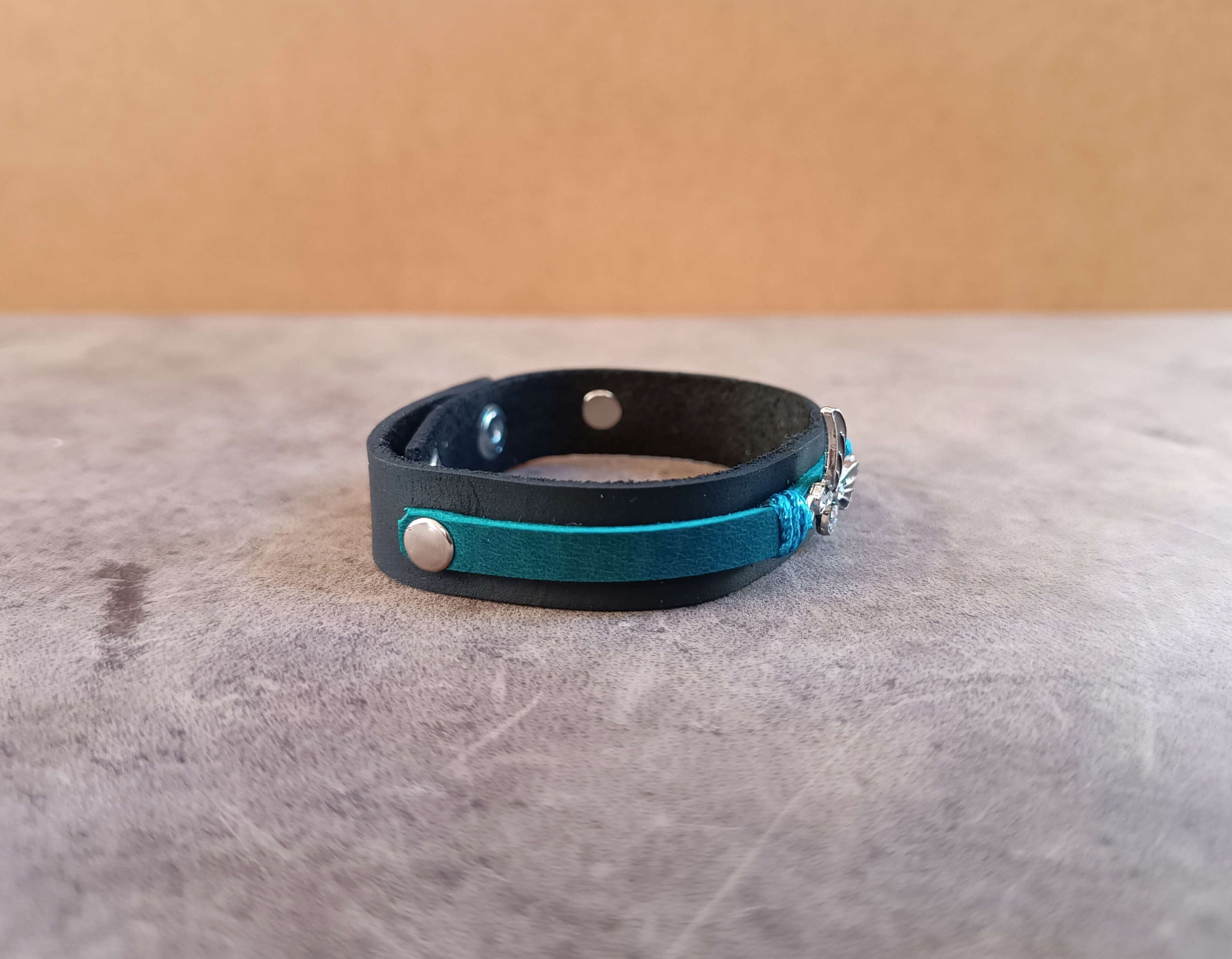 Black leather bracelet with teal accents on a gray surface