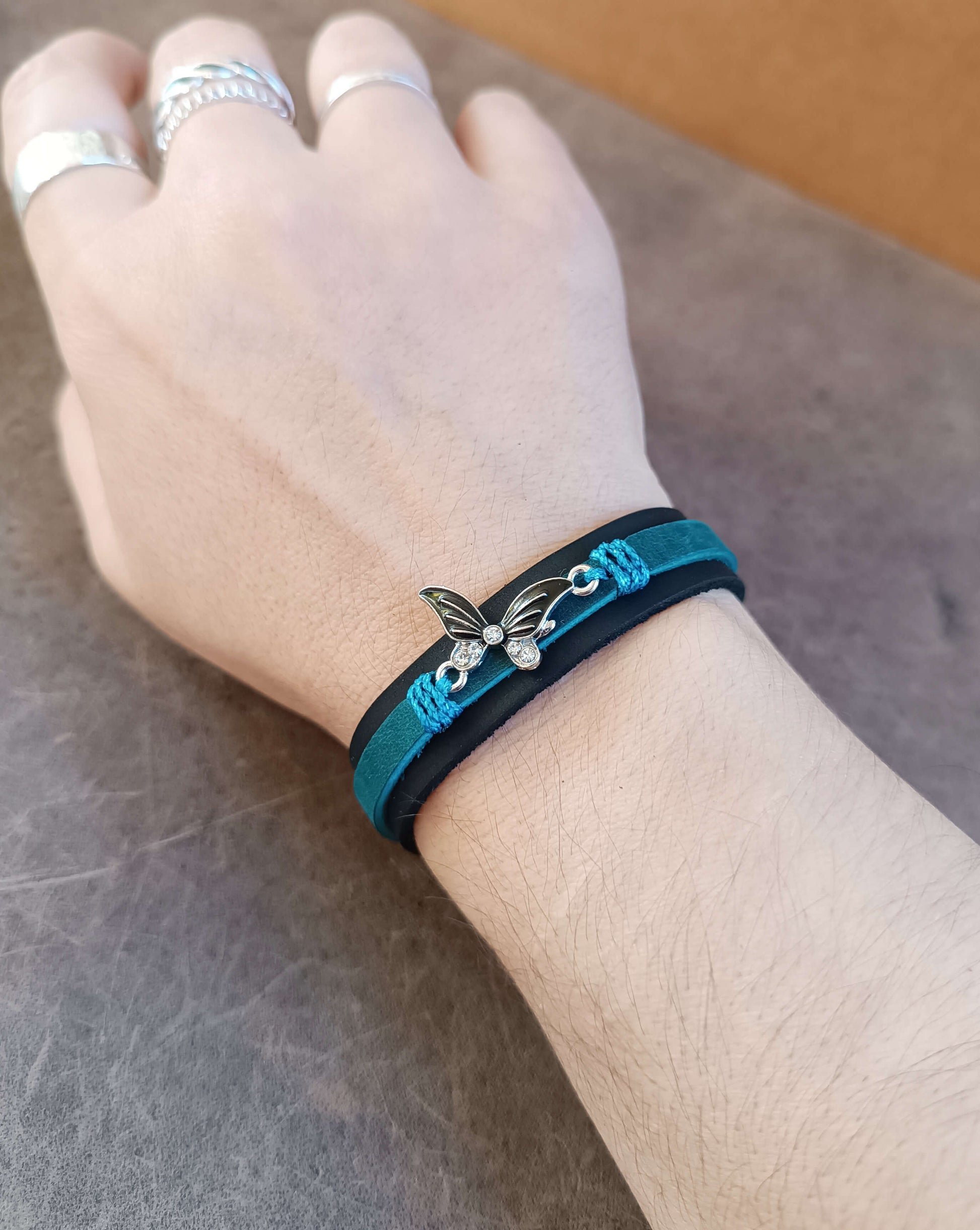 Hand wearing a blue and black bracelet with a butterfly charm on a neutral background
