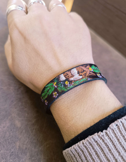 Hand wearing a colorful bracelet with nature-themed design on a wooden surface
