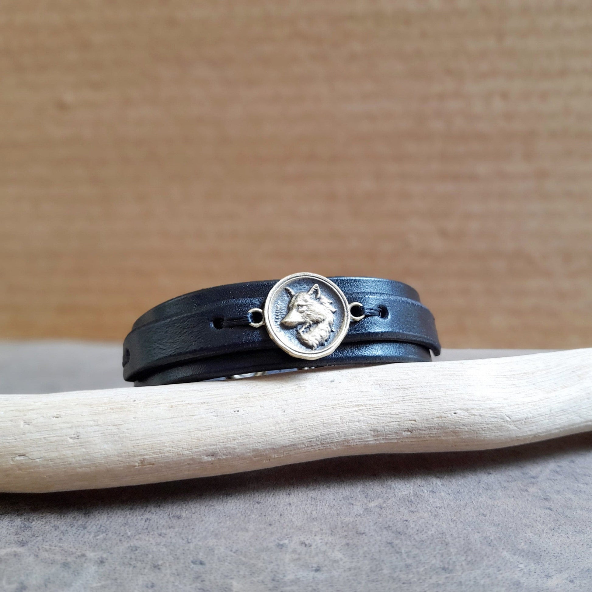 A black leather bracelet with a silver 925 Nordic wolf pendant, displayed on a wooden stand.