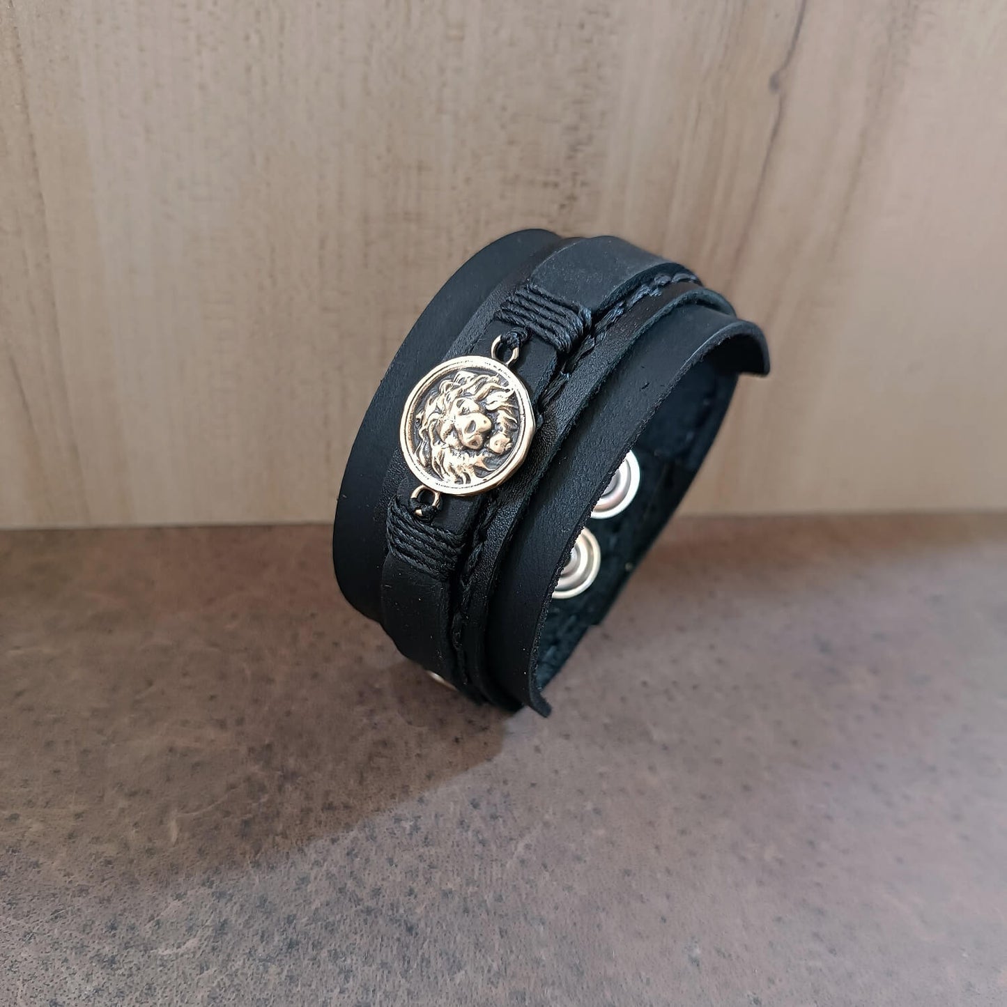 Black leather bracelet with lion pendant on a wooden surface