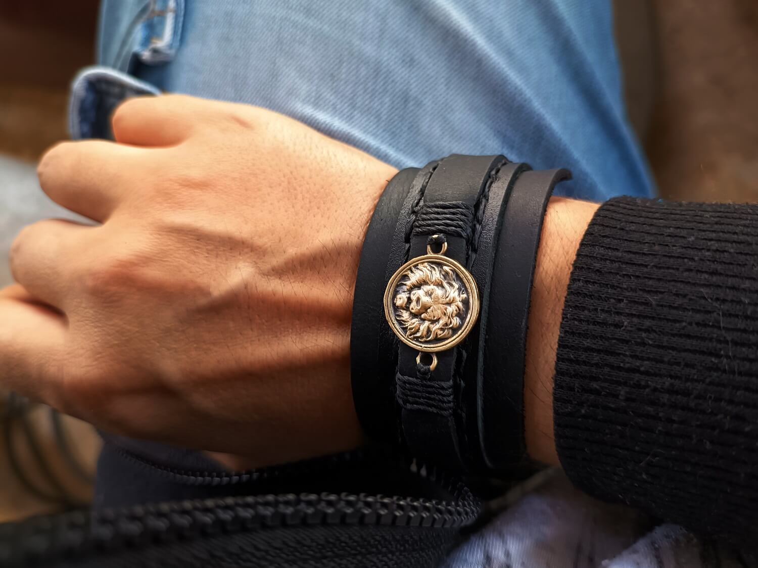 Close-up of a hand wearing a black leather bracelet with a lion emblem on a blurred background.
