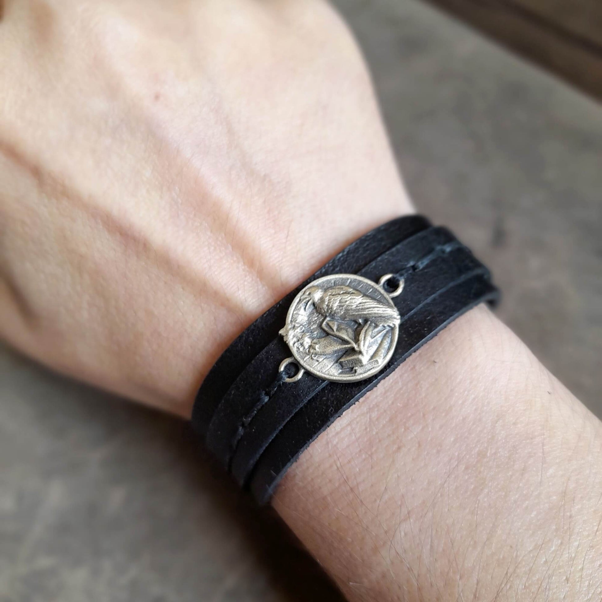 Black leather bracelet with a brass pendant emblem on a wrist