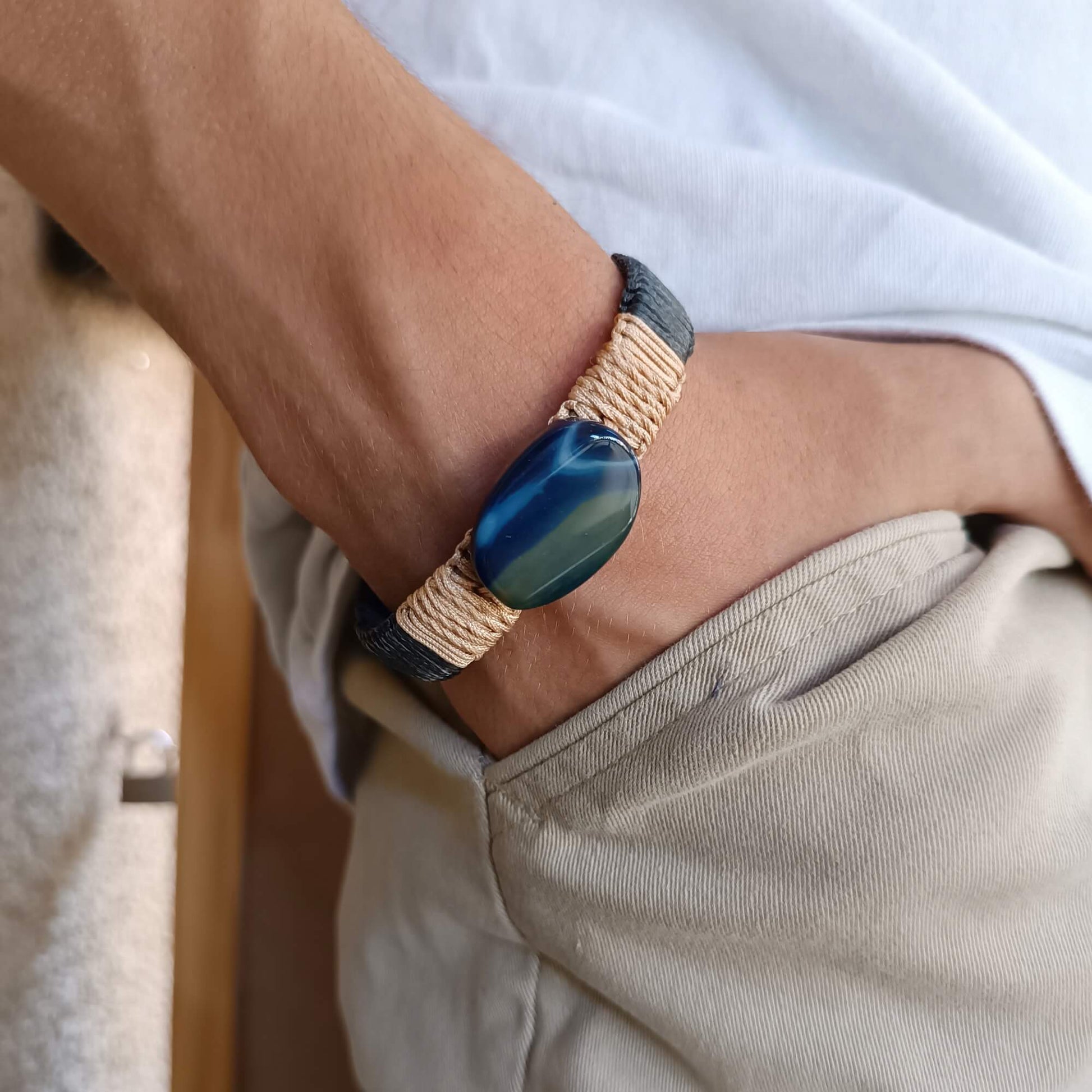 Close-up of a man's wrist wearing a leather bracelet with a blue agate stone on a neutral background