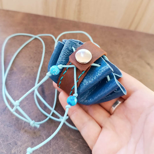 Hand holding a blue and brown mini leather neck pouch with beads, showcasing its tiny size and drawstring closure with the secure snap button.